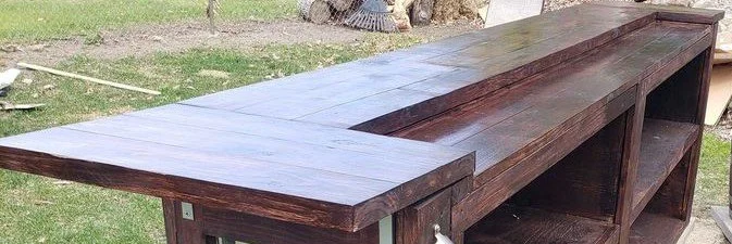 A wooden outdoor table with built-in storage, placed on a grassy area.