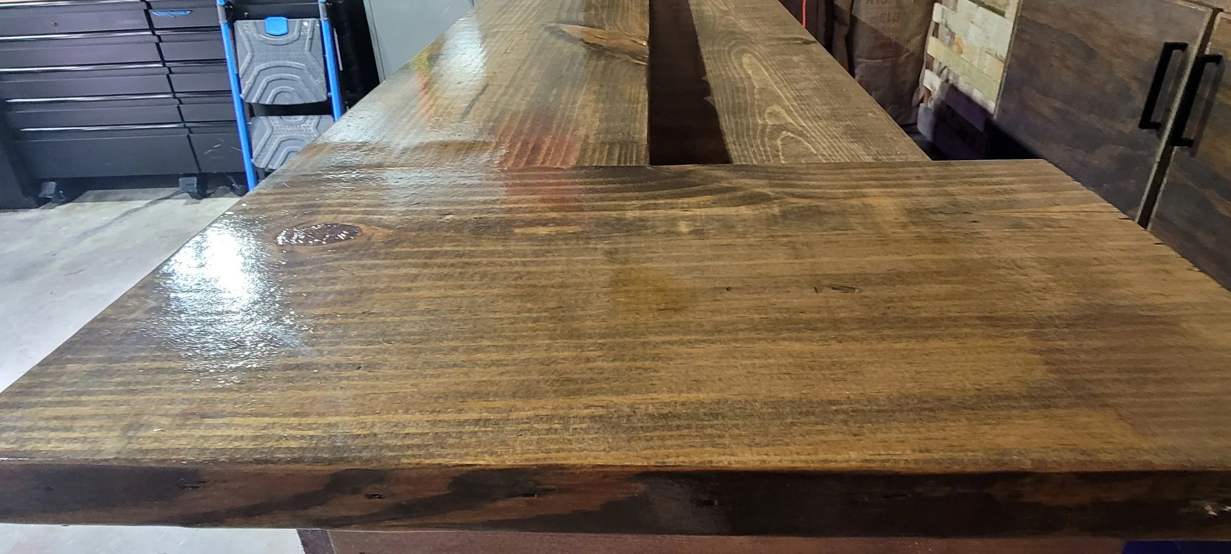 A large wooden table in a garage or workshop setting with a polished surface that reflects light.