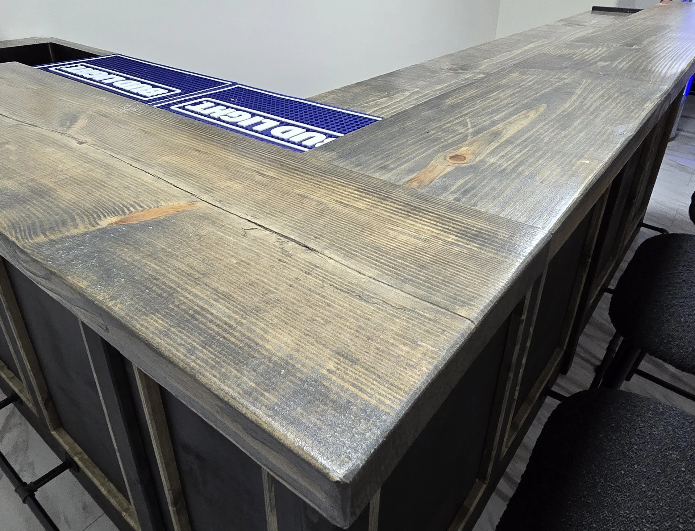 A wooden bar counter with two blue rubber mats that have white text, likely in a bar or restaurant setting.