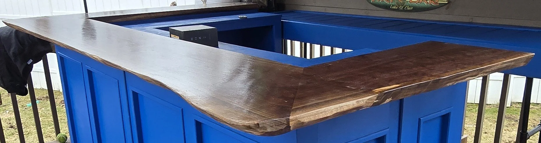 A partially assembled blue bar counter with a wooden top on a porch or deck.