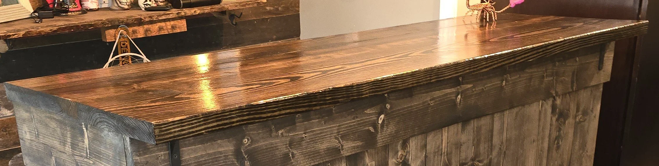 Wooden bar counter with a polished top and rustic paneling underneath in a bar or restaurant setting.