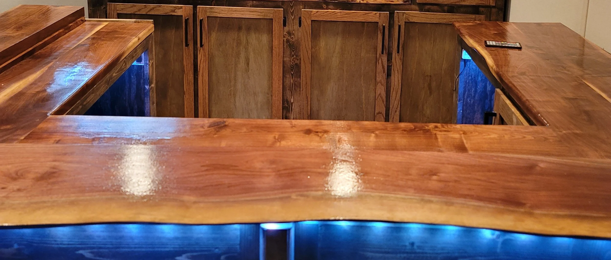Wooden bar counter with a remote control on top and blue lighting underneath.