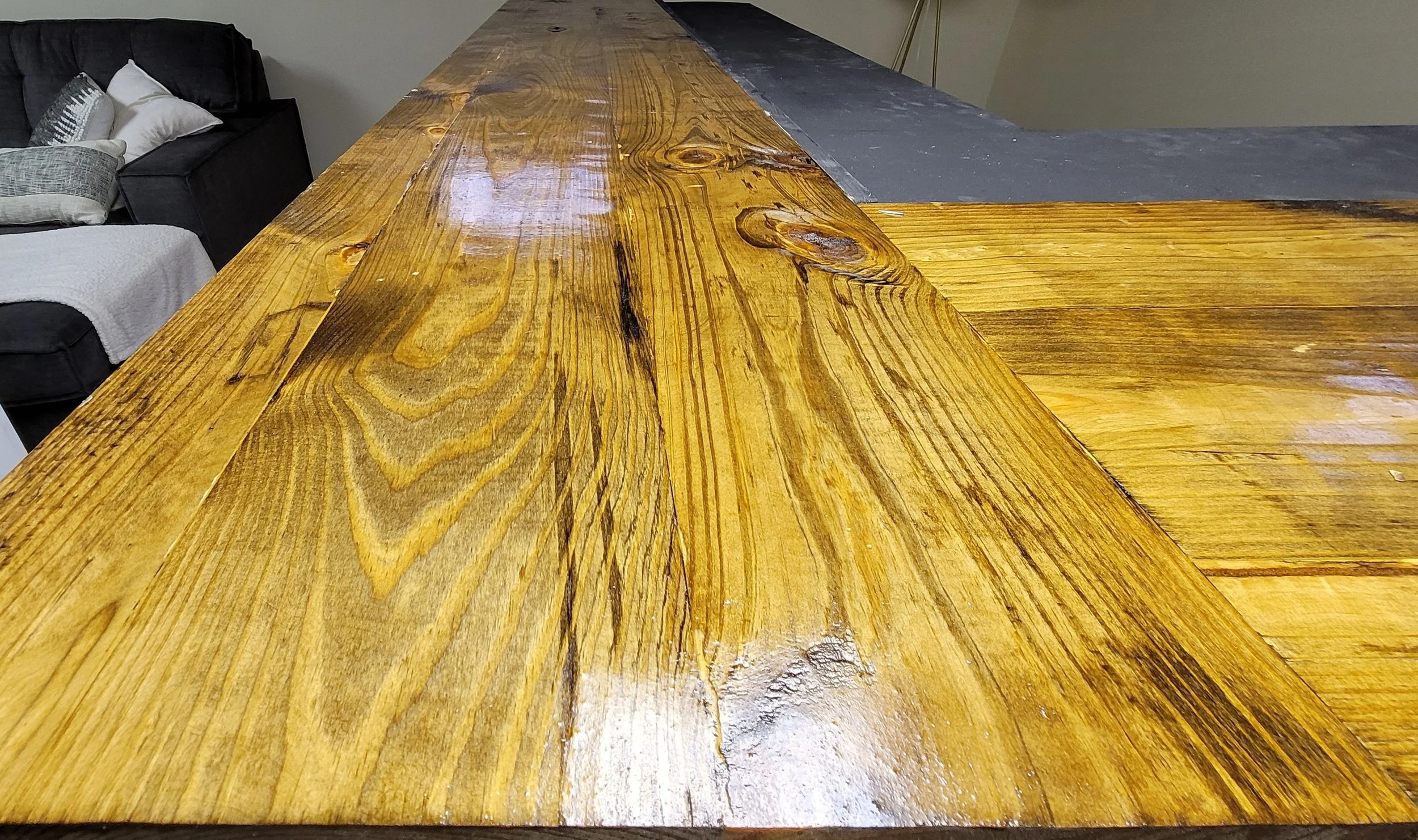 Close-up of a wooden tabletop with a natural finish, showcasing wood grain and knots, with parts covered by a black surface.
