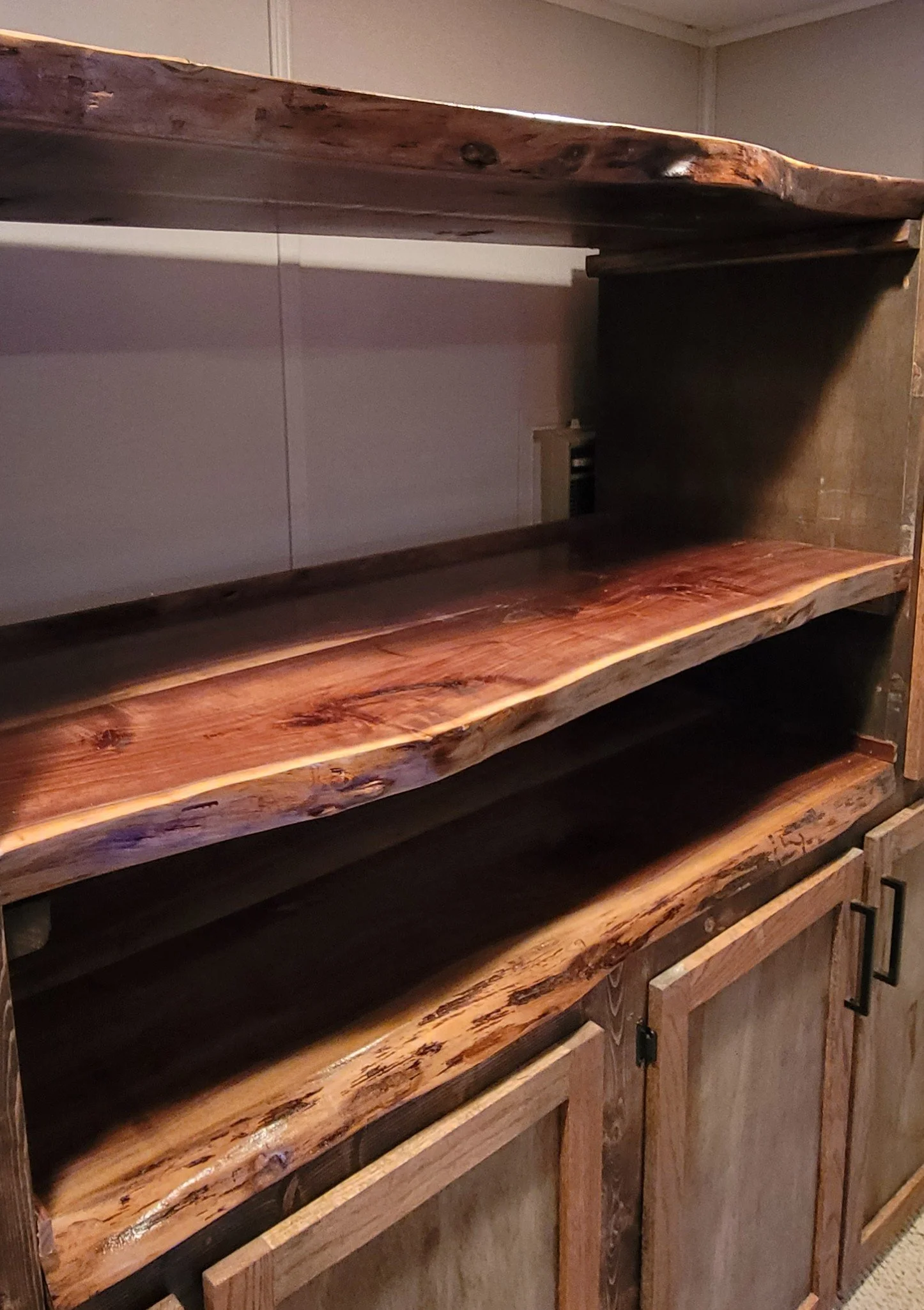 A wooden kitchen island with a natural, rustic finish, placed against a beige wall, with cabinets below and no countertop appliances visible.
