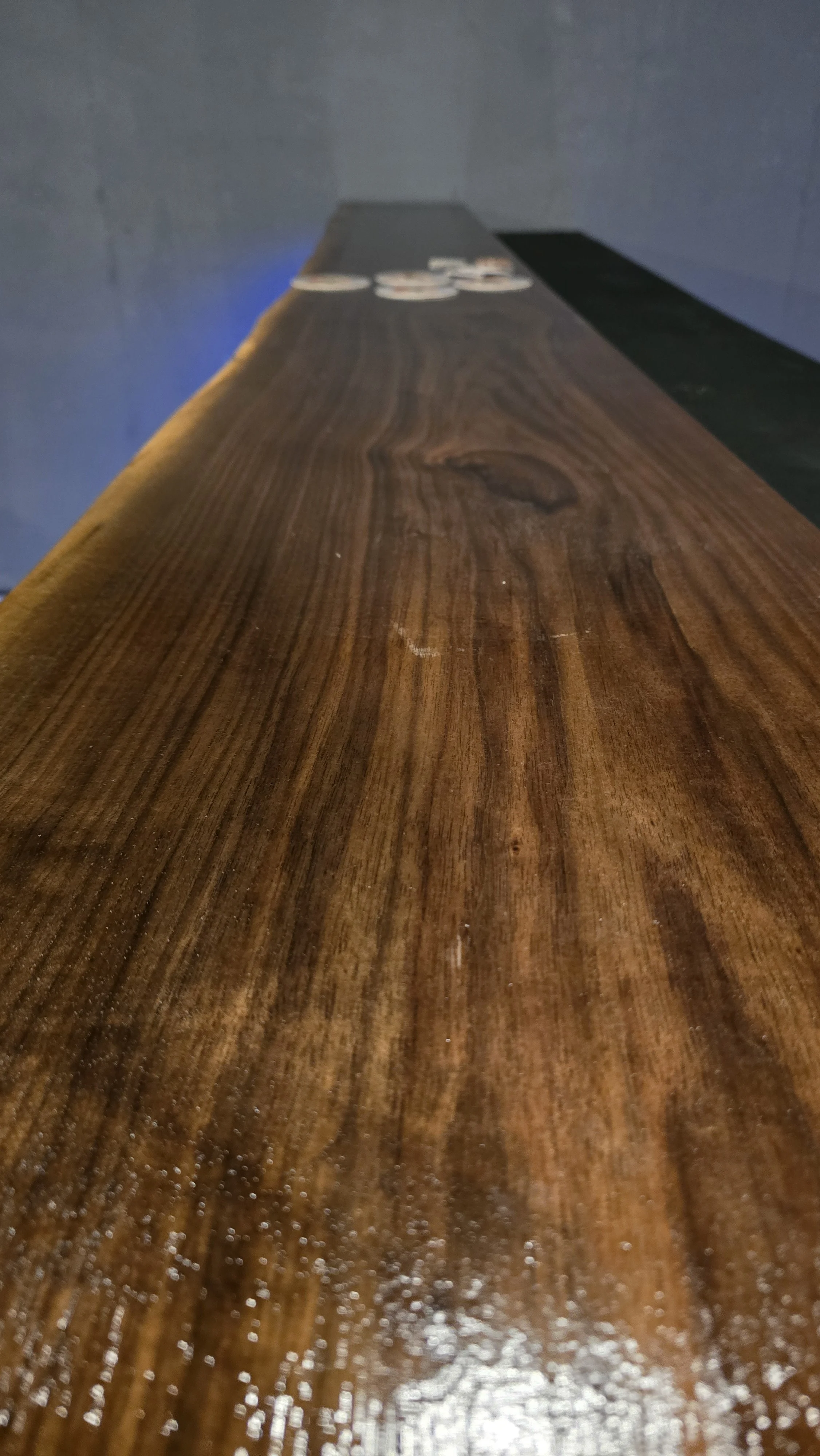 Close-up of a polished wooden surface with a dark brown finish, showing wood grain and knots, with some white powder or dust at the bottom edge.