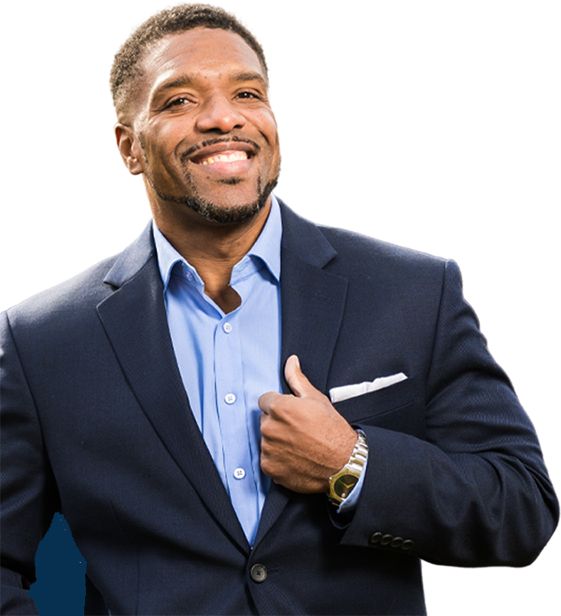 A smiling man in a navy blue suit with a light blue shirt, adjusting his suit jacket, standing against a blurred background.