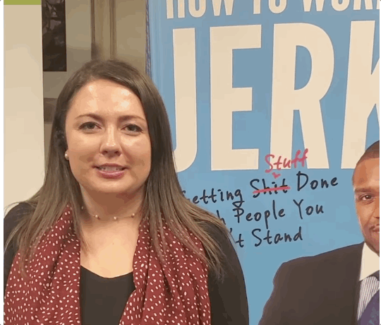 A woman with brown hair wearing a black shirt and red polka dot scarf standing in front of a blue sign that reads 'How to Work Jerk' with some handwritten notes overlayed.