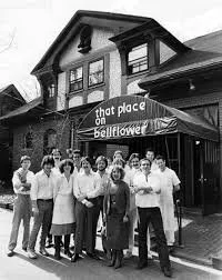 A group of people standing in front of a historic building with a sign that reads 'that place on Beallflower,' above the entrance.