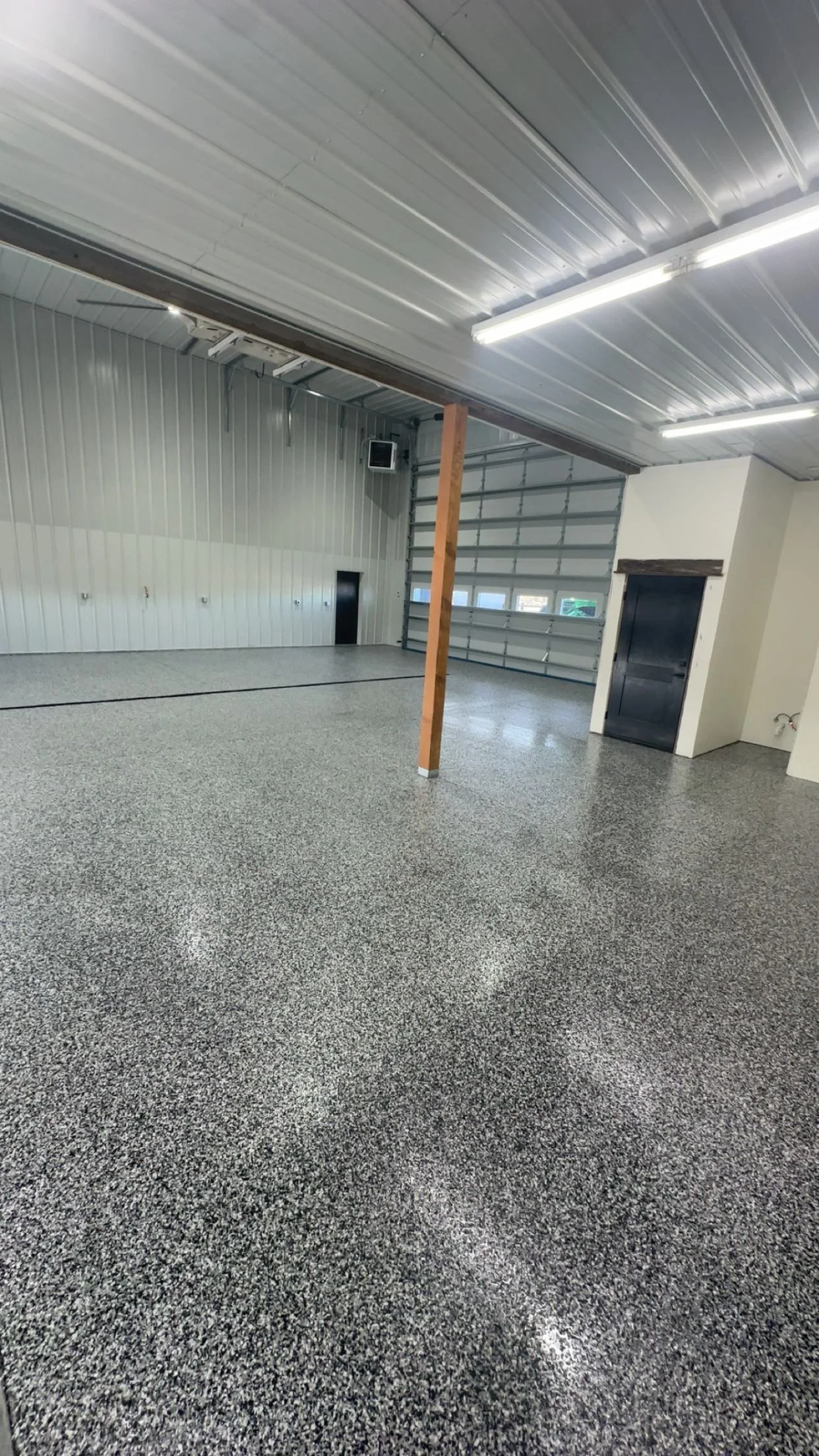 Empty garage with polished concrete floor, metal ceiling, and large garage doors, with a vertical wooden support beam.