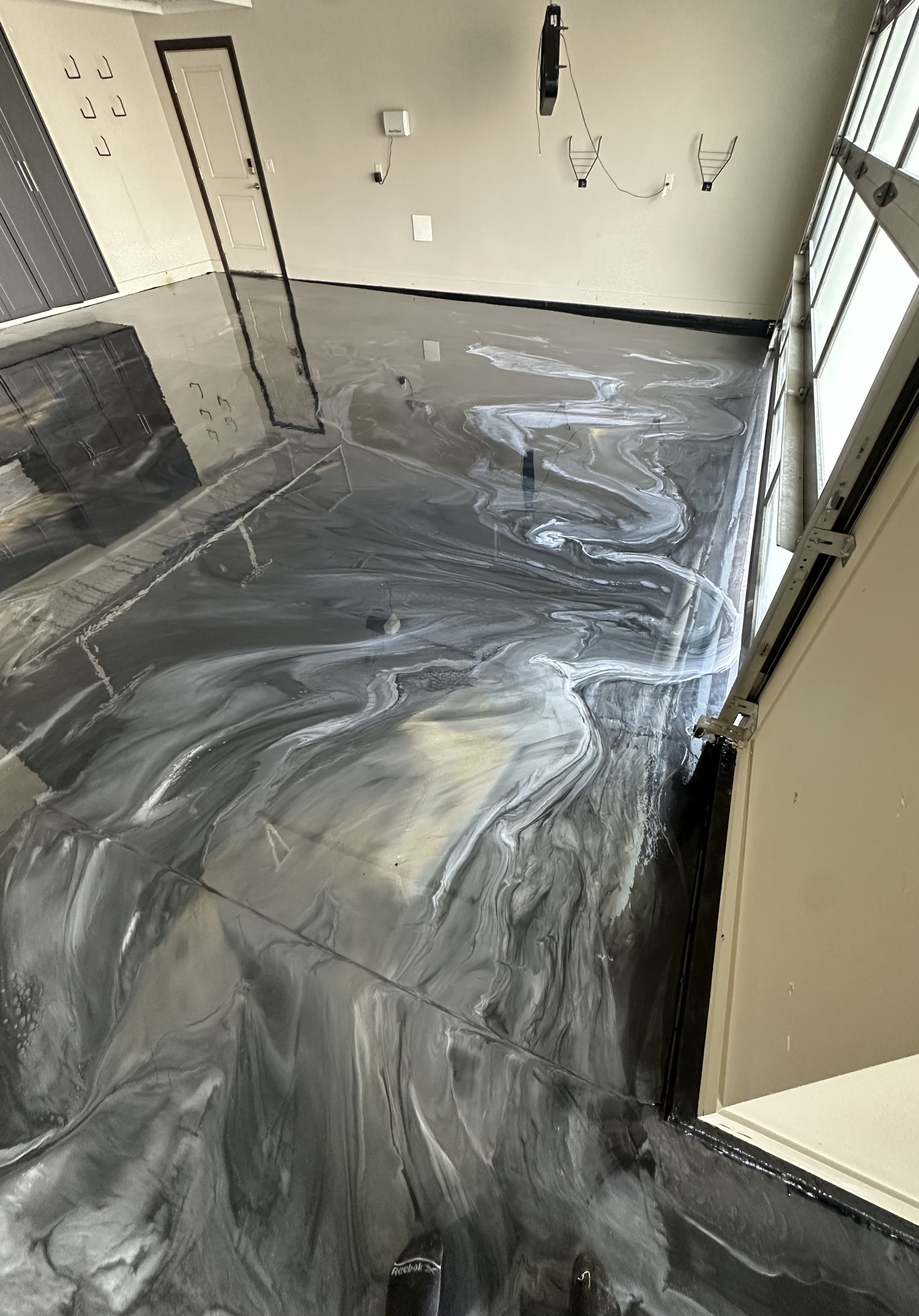 Empty garage with freshly poured black and gray marble epoxy floor, reflecting the ceiling and door.