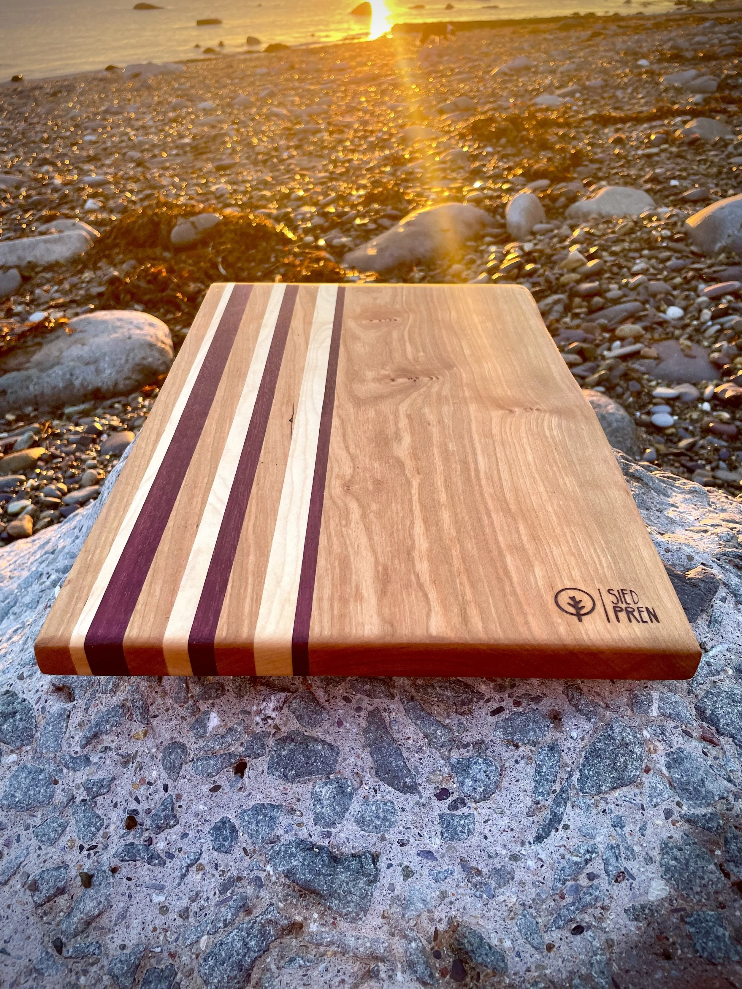 A wooden cutting board with striped pattern on a rocky surface near a beach during sunset.