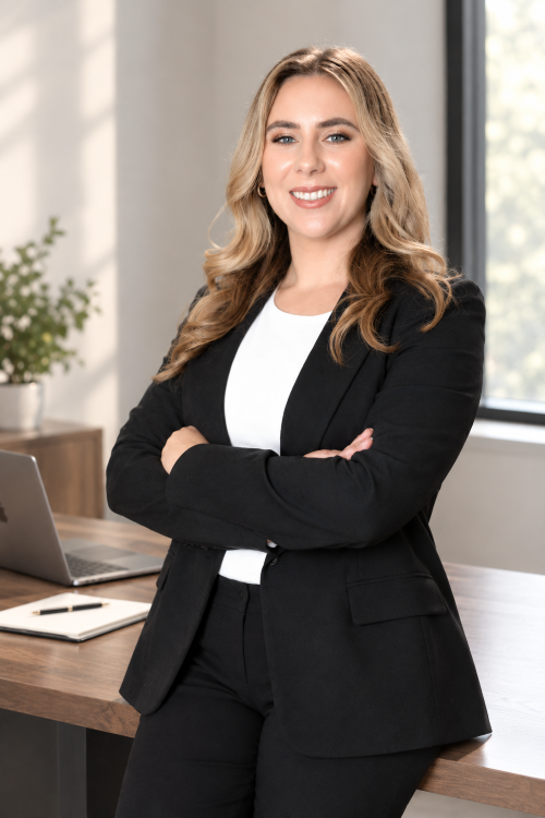 Dr. Jessica Roos in a black suit standing with folded arms and smiling in a modern office