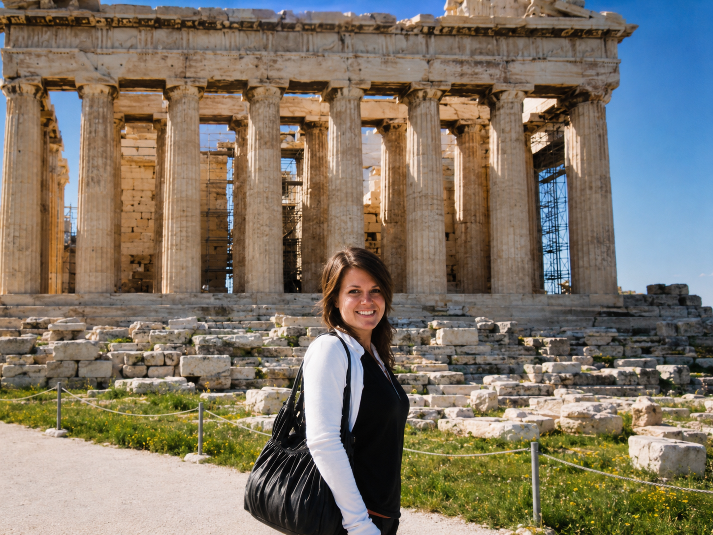 A woman smiling at the camera standing in front of the ancient Parthenon temple ruins on a sunny day.