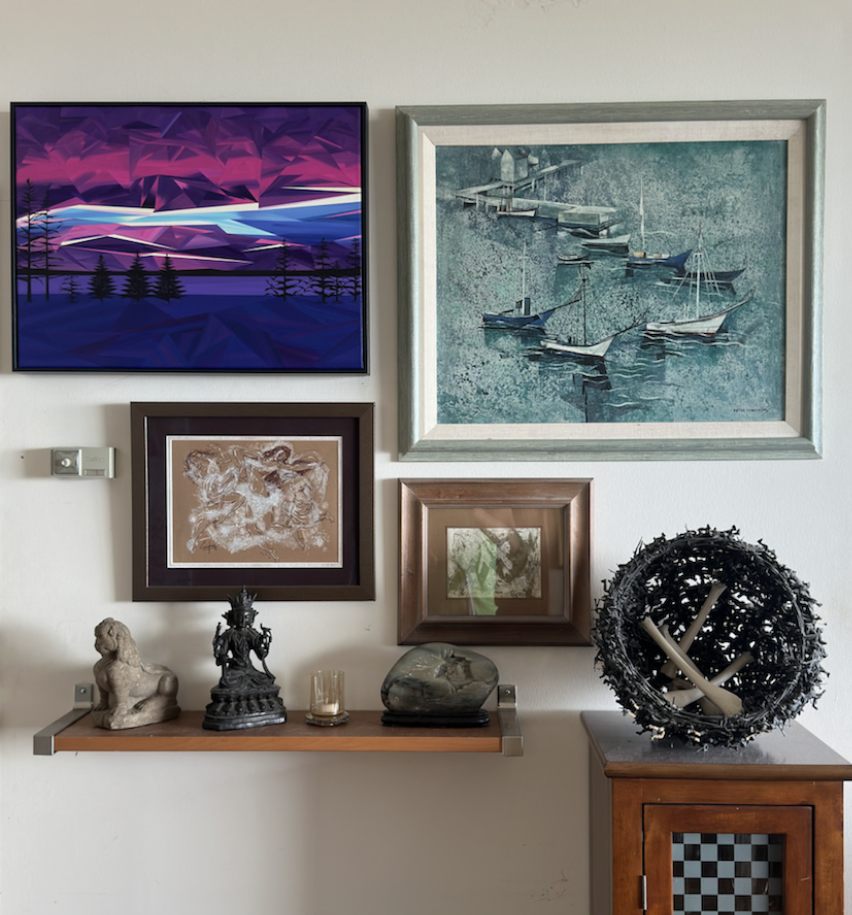 Purple and blue geometric landscape painting displayed among a collection of framed artwork in a home.