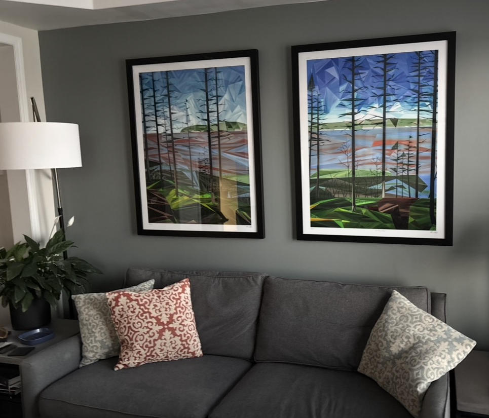 Two framed geometric forest landscapes displayed side by side above a grey sofa in a living room.