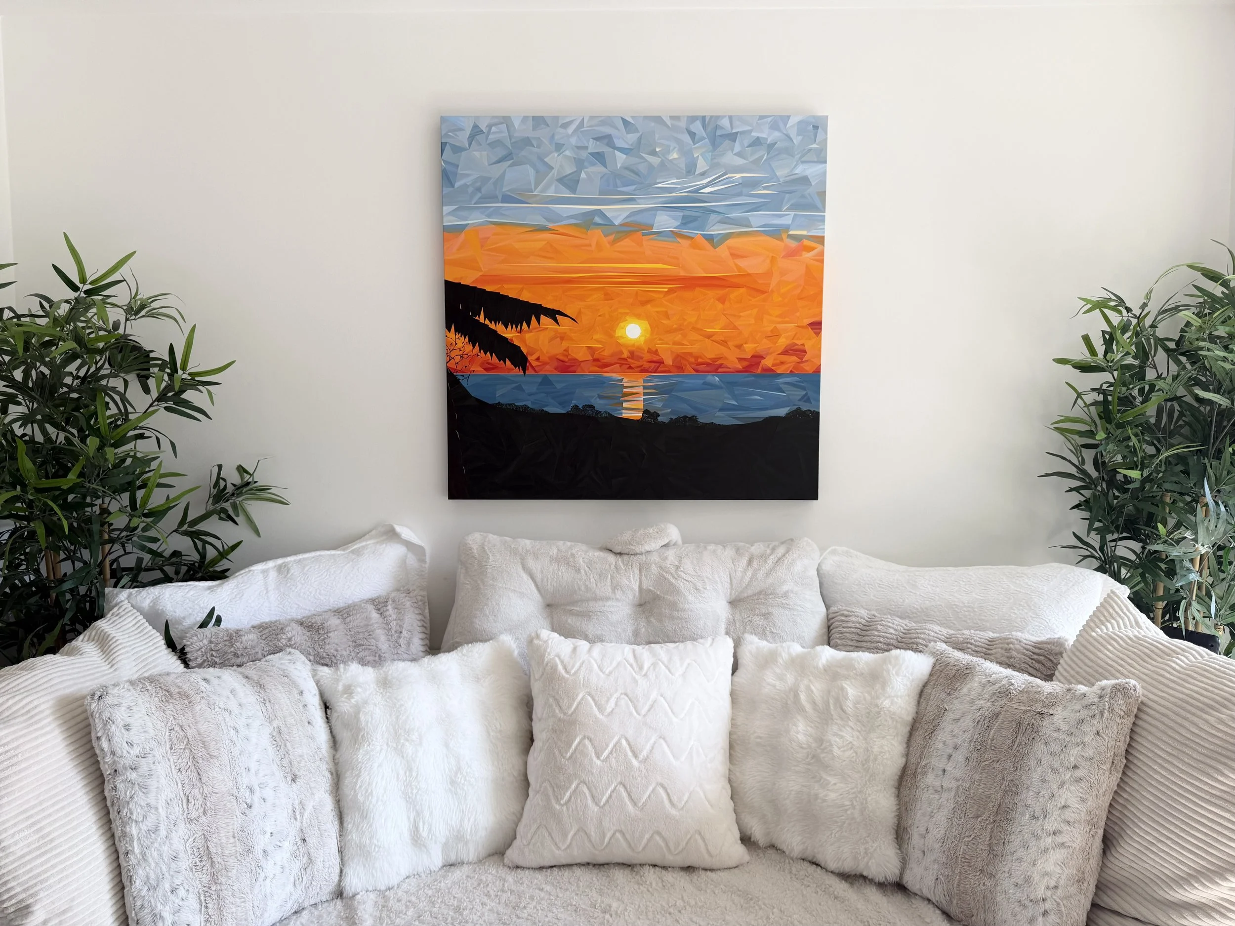 Colourful geometric sunset painting displayed above a white sofa in a bright, neutral living space.