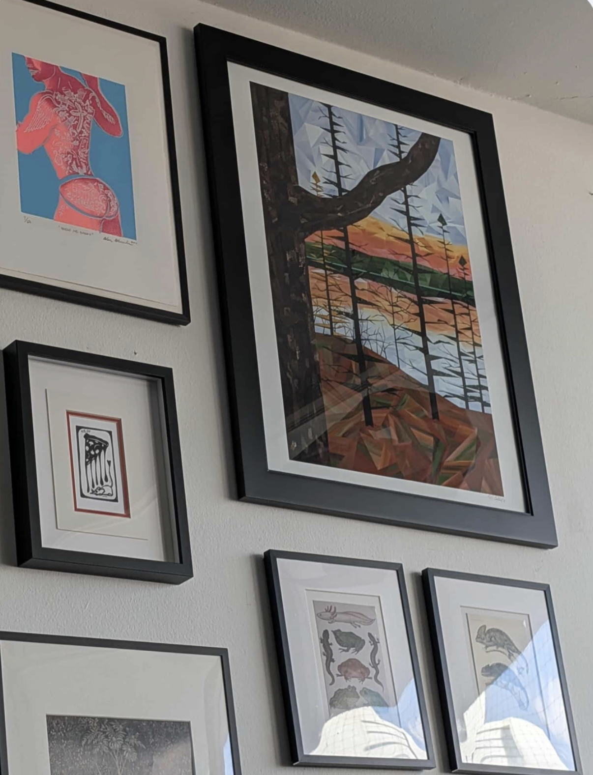 Large framed geometric forest landscape featuring tall dark trees, water and warm sunset tones, displayed as part of an eclectic gallery wall in a client’s home.