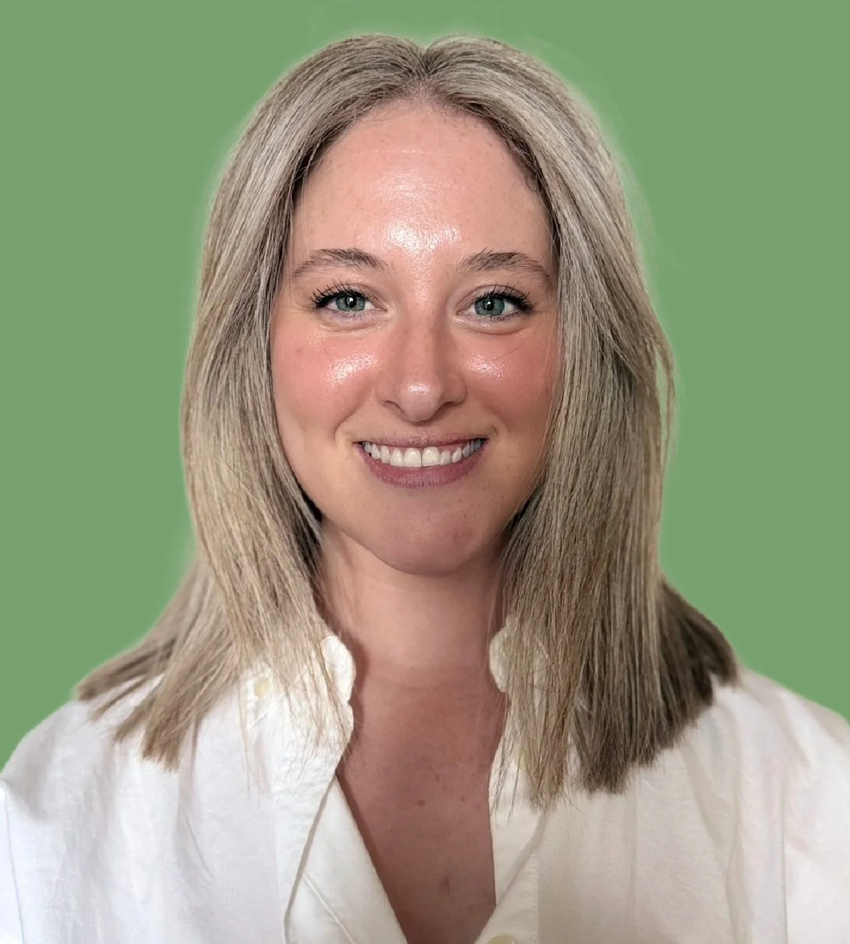 Close-up of a woman with shoulder-length blonde hair, blue eyes, and a bright smile, wearing a white shirt, against a solid green background.