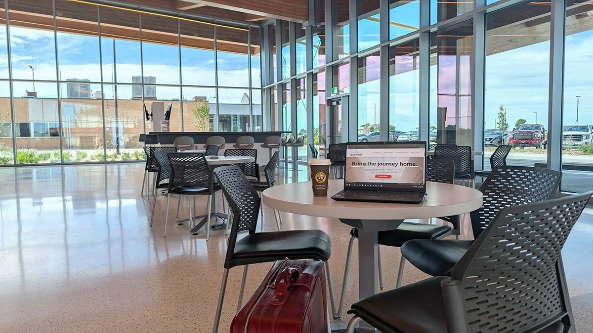 An interior view of North Platte Regional Airport's passenger terminal is seen. In the foreground, a laptop and a coffee cup are on top of a small table.