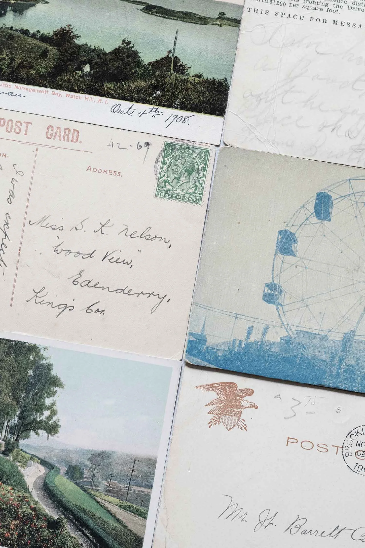 A collection of vintage postcards, including one with a black and white photo of a waterway, trees, and a pole, dated October 4th, 1908, and another with a blue Ferris wheel illustration. The postcards are partially overlapping, showcasing handwritten addresses, stamps, and postmarks.