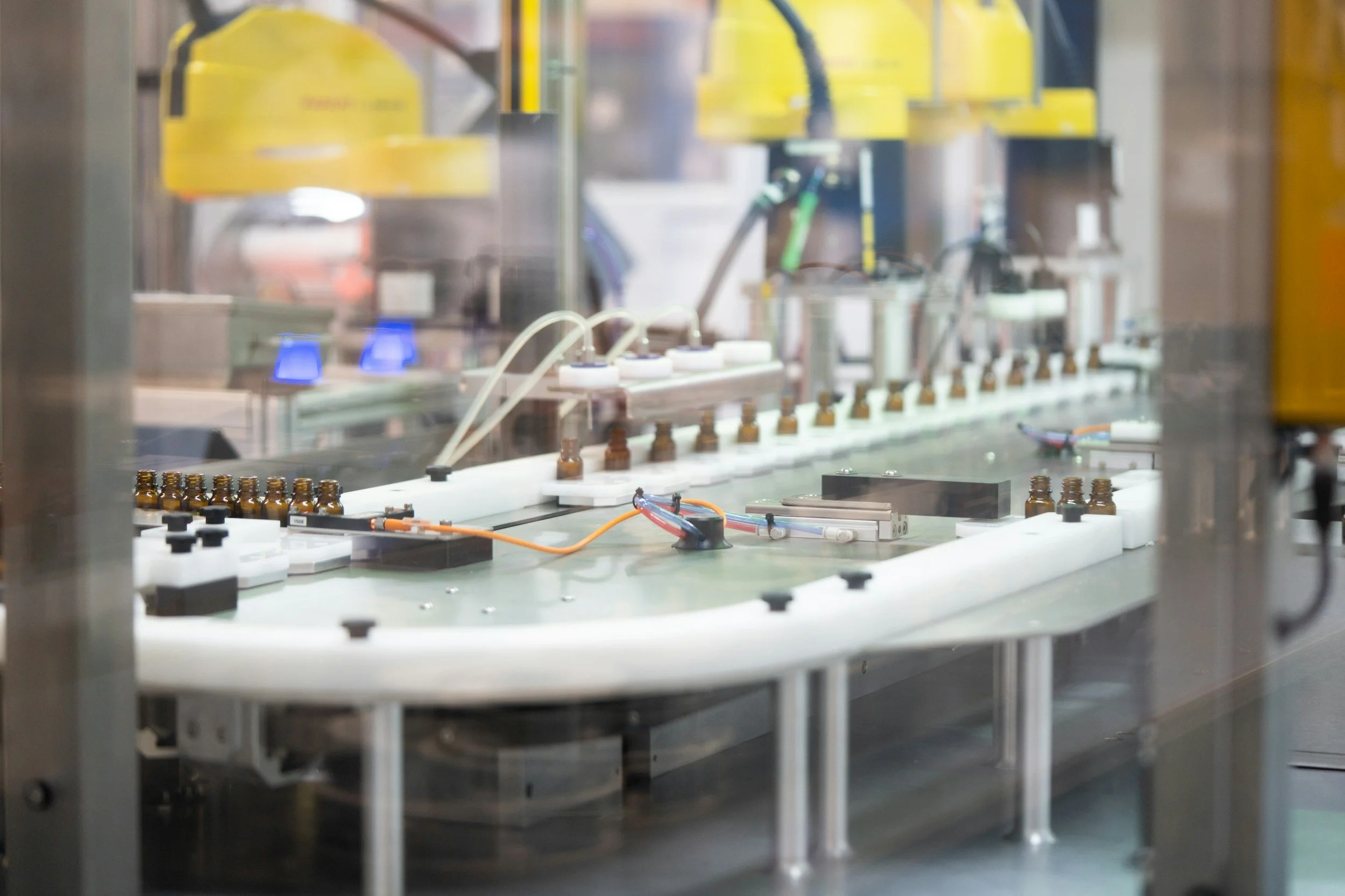 A close-up view of an automated industrial machine with conveyor belts, bottles, and robotic arms, likely part of a manufacturing or packaging process.