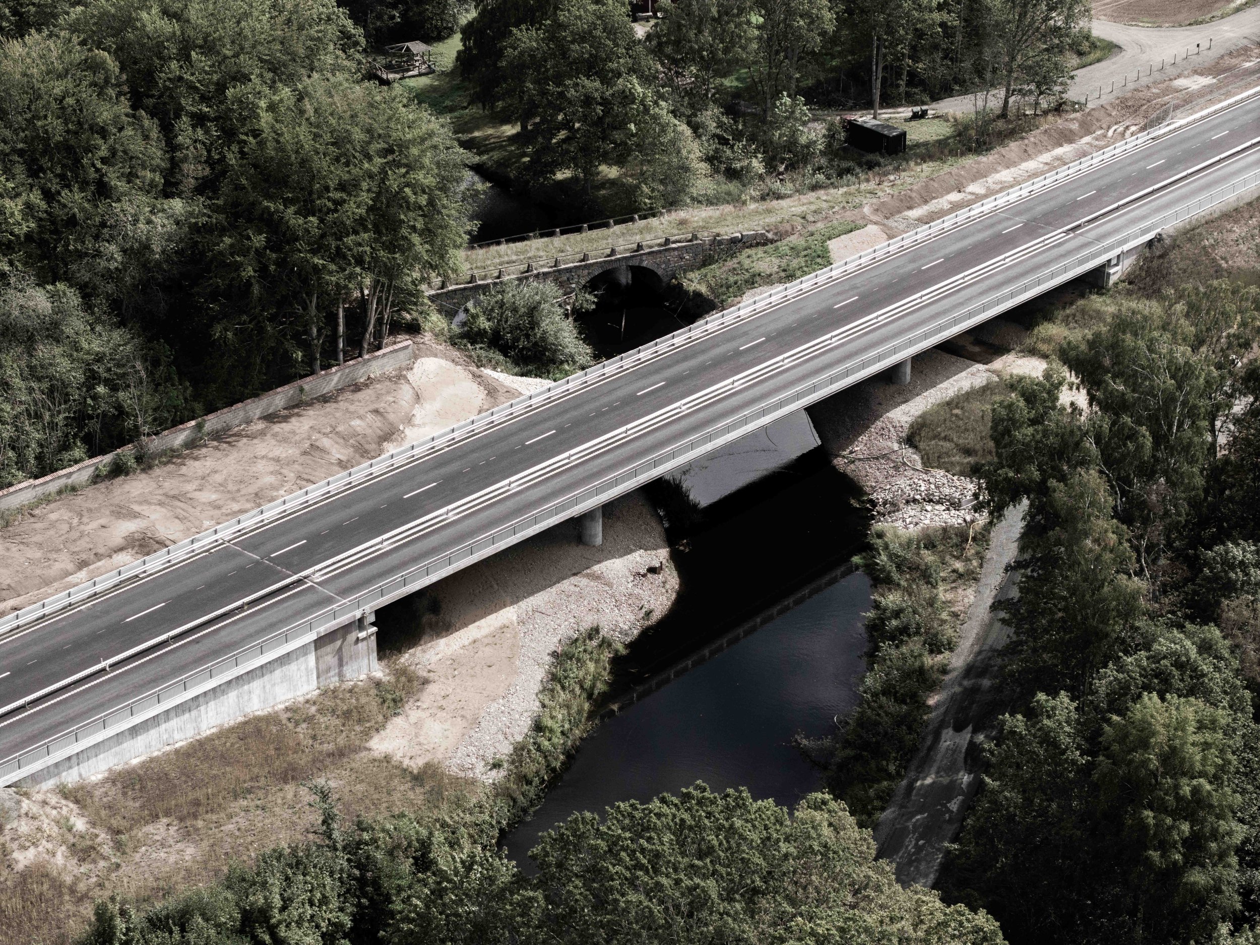 Flygbild av en bro över en flod i ett grönt skogsområde.