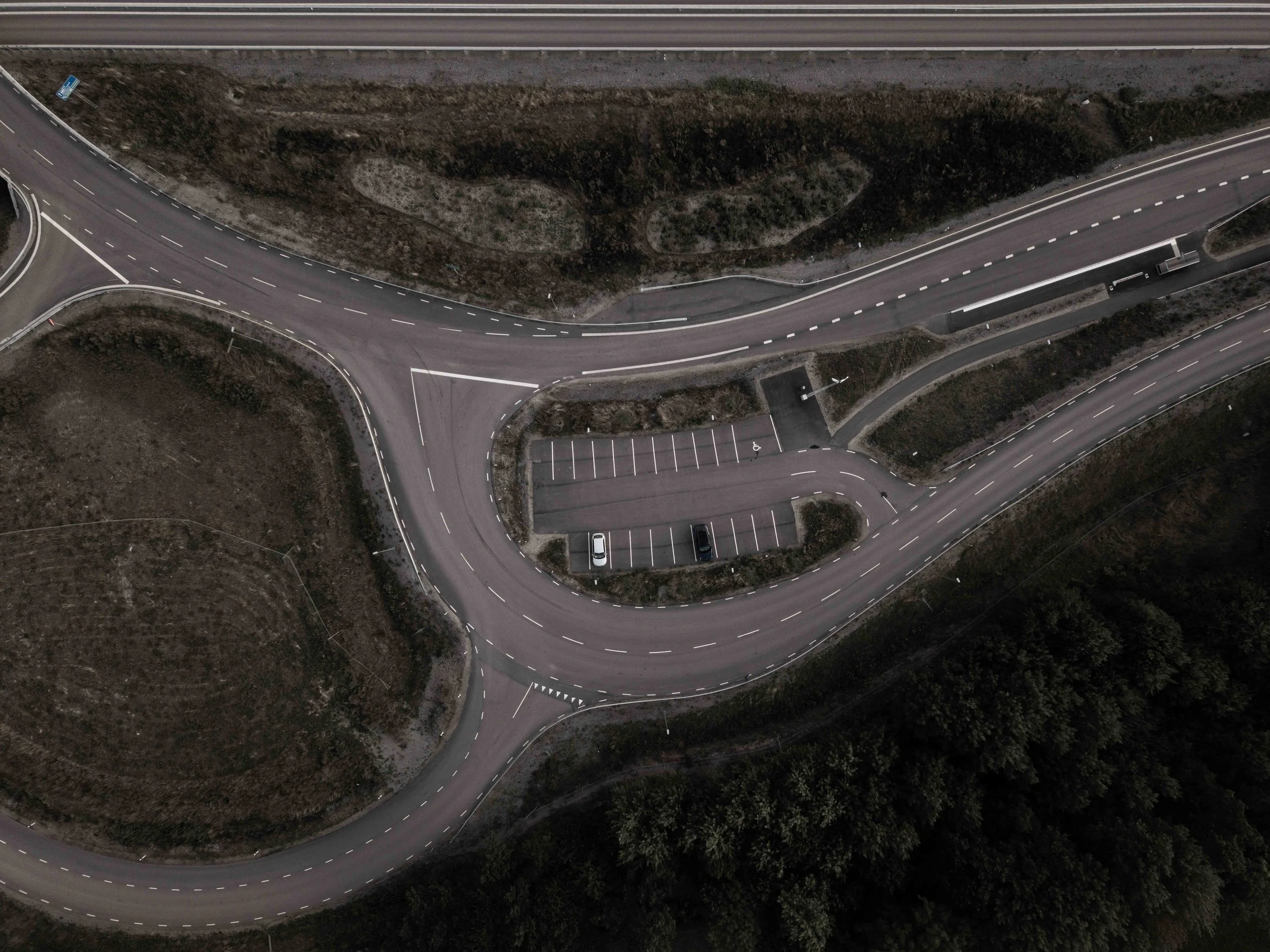 Luftbild av en böjd väg med parkeringsplatser och omgivande landskap.