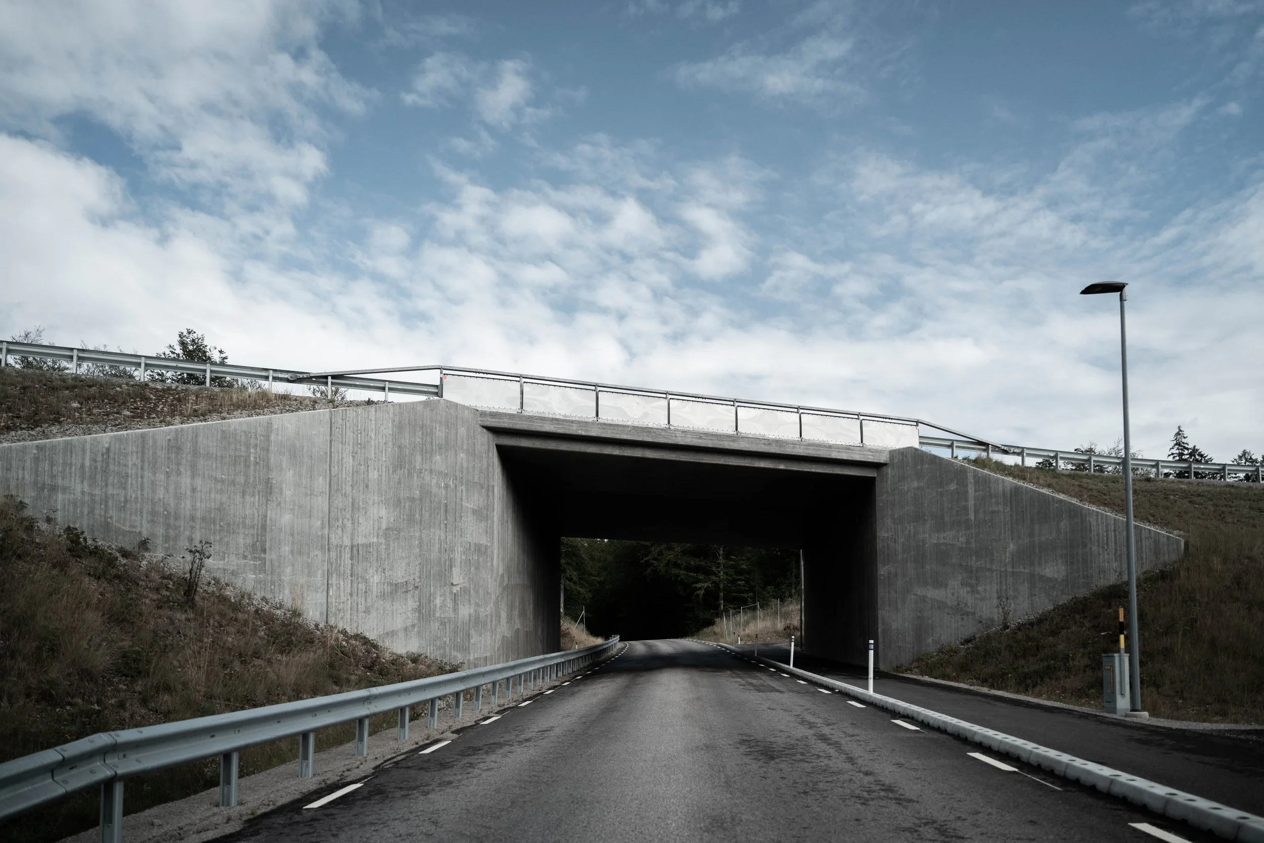 Vägundergång med tunnel under en bro och omgivande väggar samt en höjdpunktslyktakant som lyser.