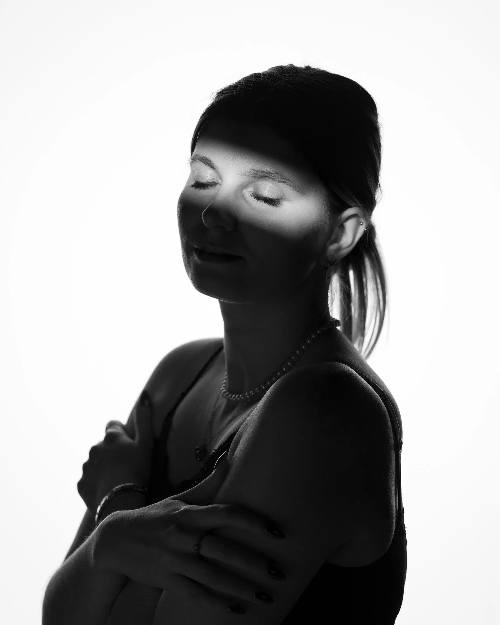 Schwarz-weiße Aufnahme eines schlafenden Mädchens mit geschlossenen Augen, getragen in einem schwarzen Tank-Top, mit dunklem Haar, das nach hinten gestylt ist, vor einem weißen Hintergrund.
