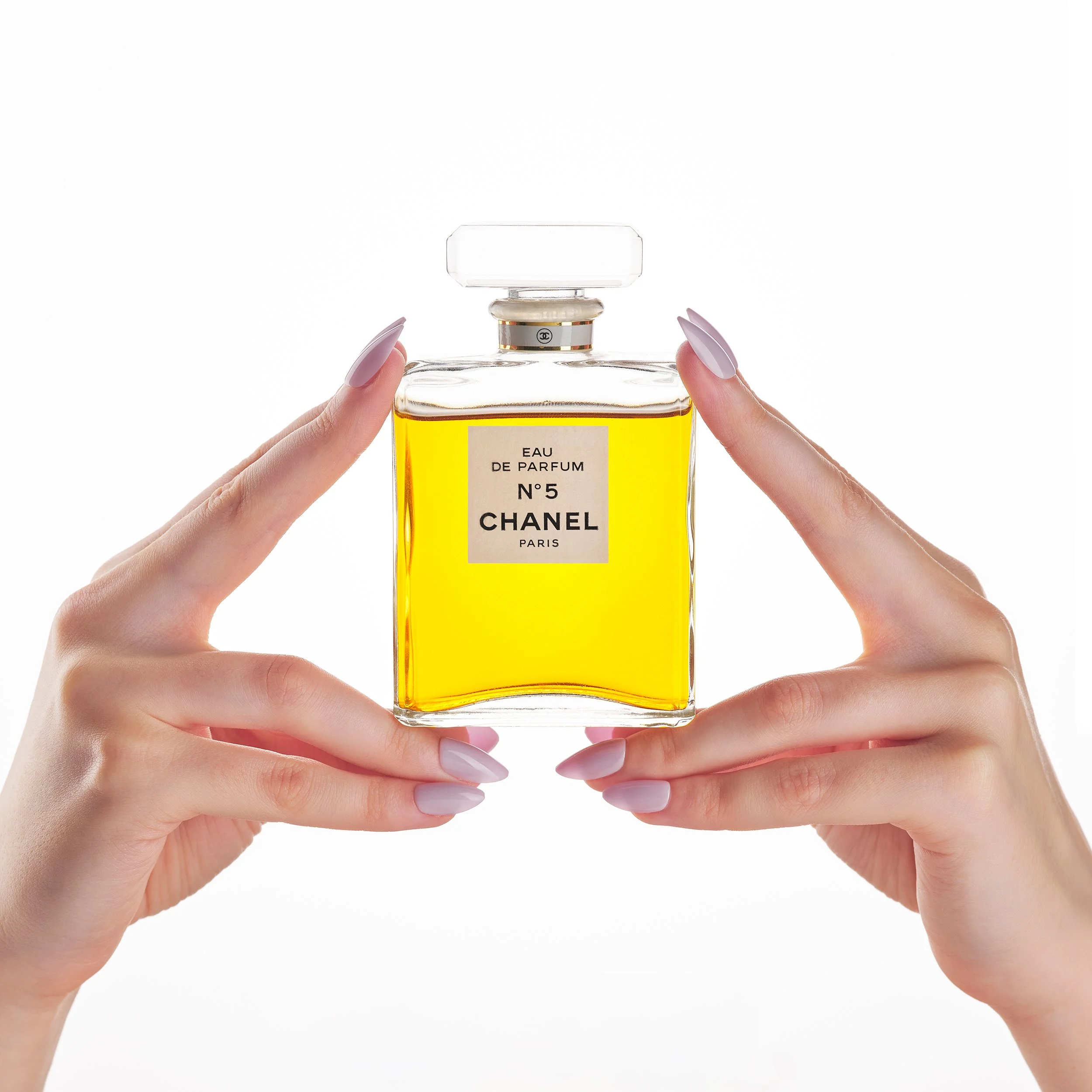 Hand hält eine Chanel Parfümflasche mit gelber Flüssigkeit vor weißem Hintergrund.