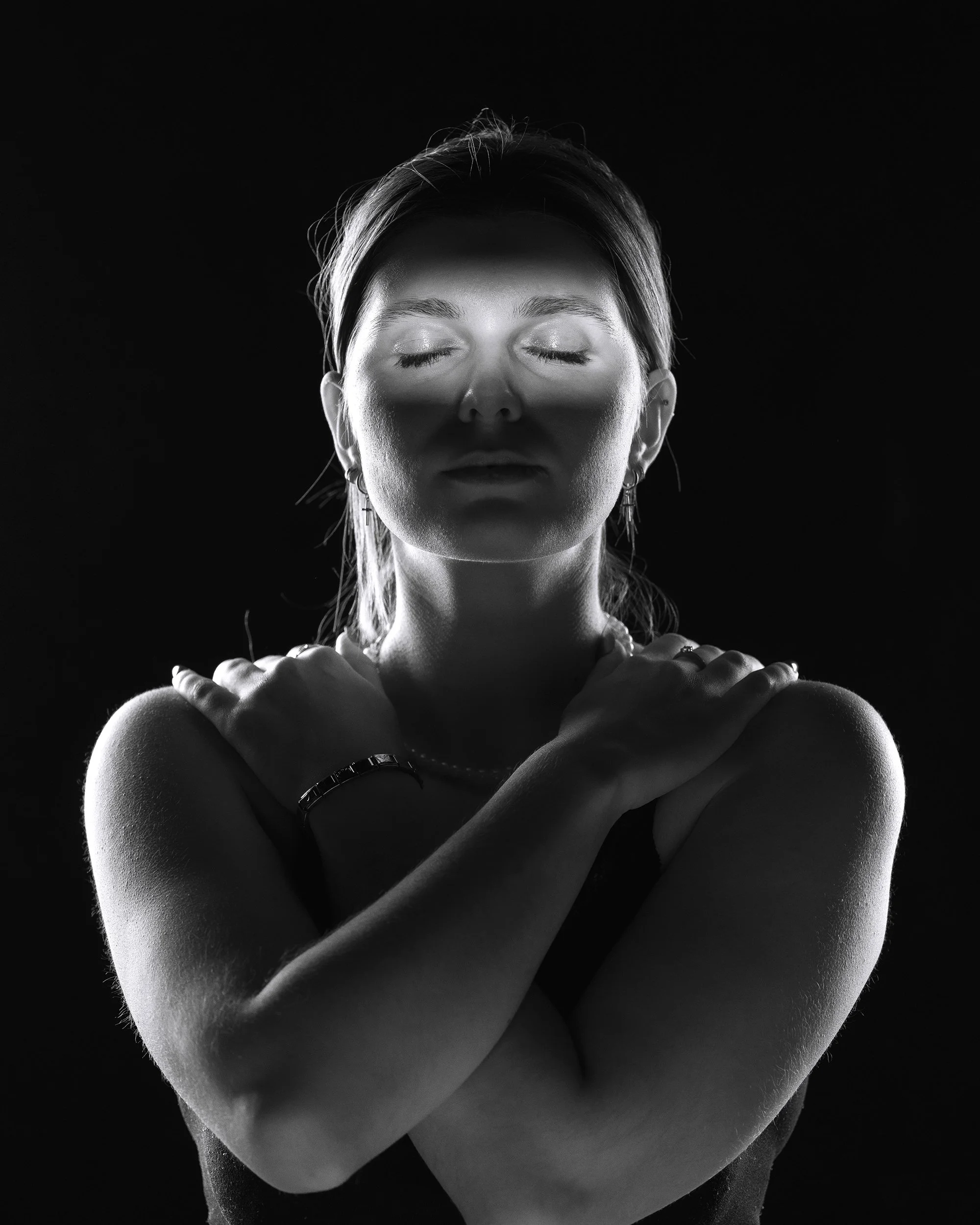 Schwarz-Weiß-Fotografie eines Frauengesichts mit geschlossenen Augen, die Arme sind vor der Brust gekreuzt.