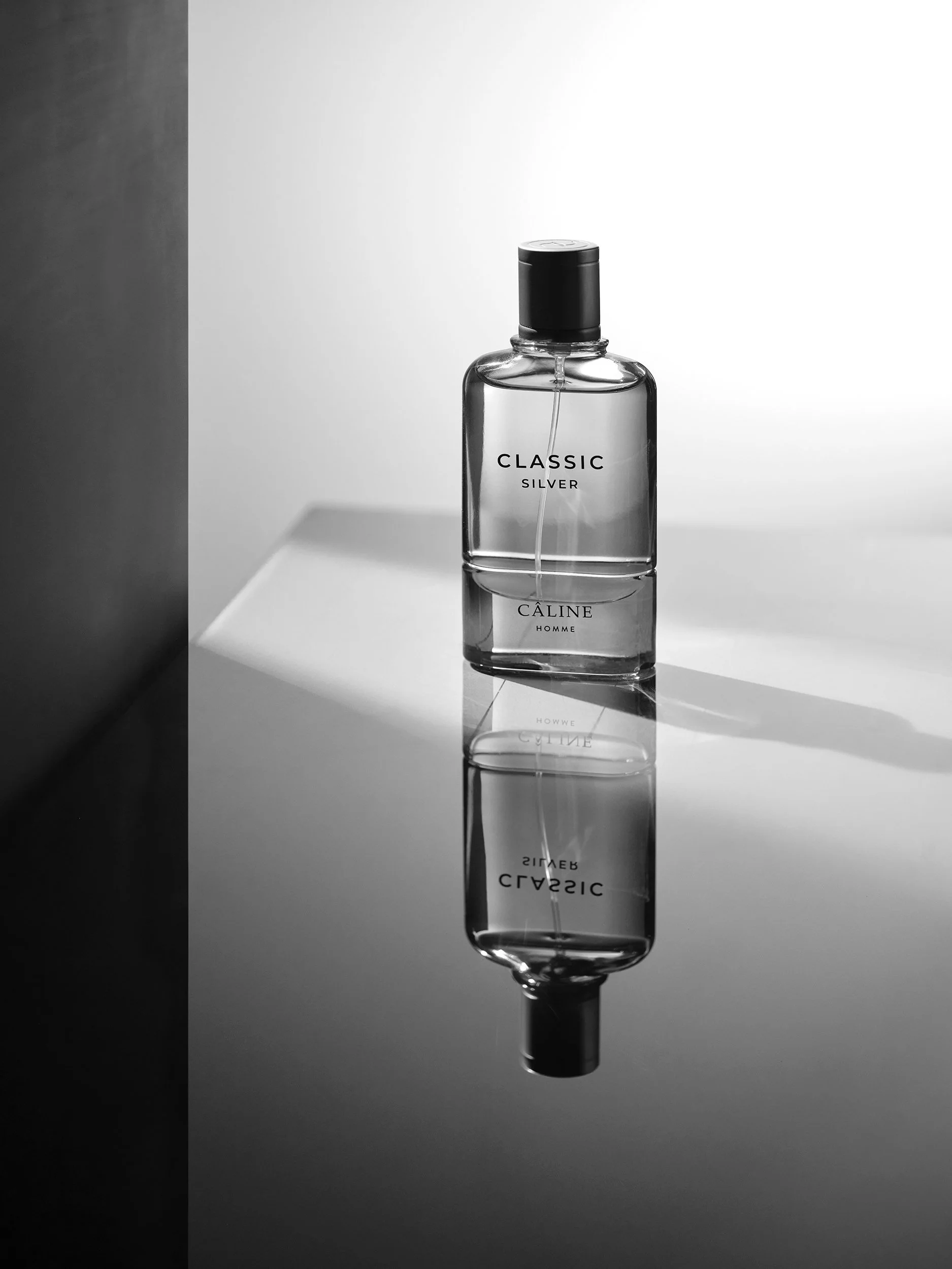 Schwarze Parfümflasche mit schwarzem Deckel, auf einem weißen Tisch, die Flasche trägt das Label "CLASSIC SILVER CALINE HOMME"; der Hintergrund ist in Schwarz, Weiß und Grau gehalten.