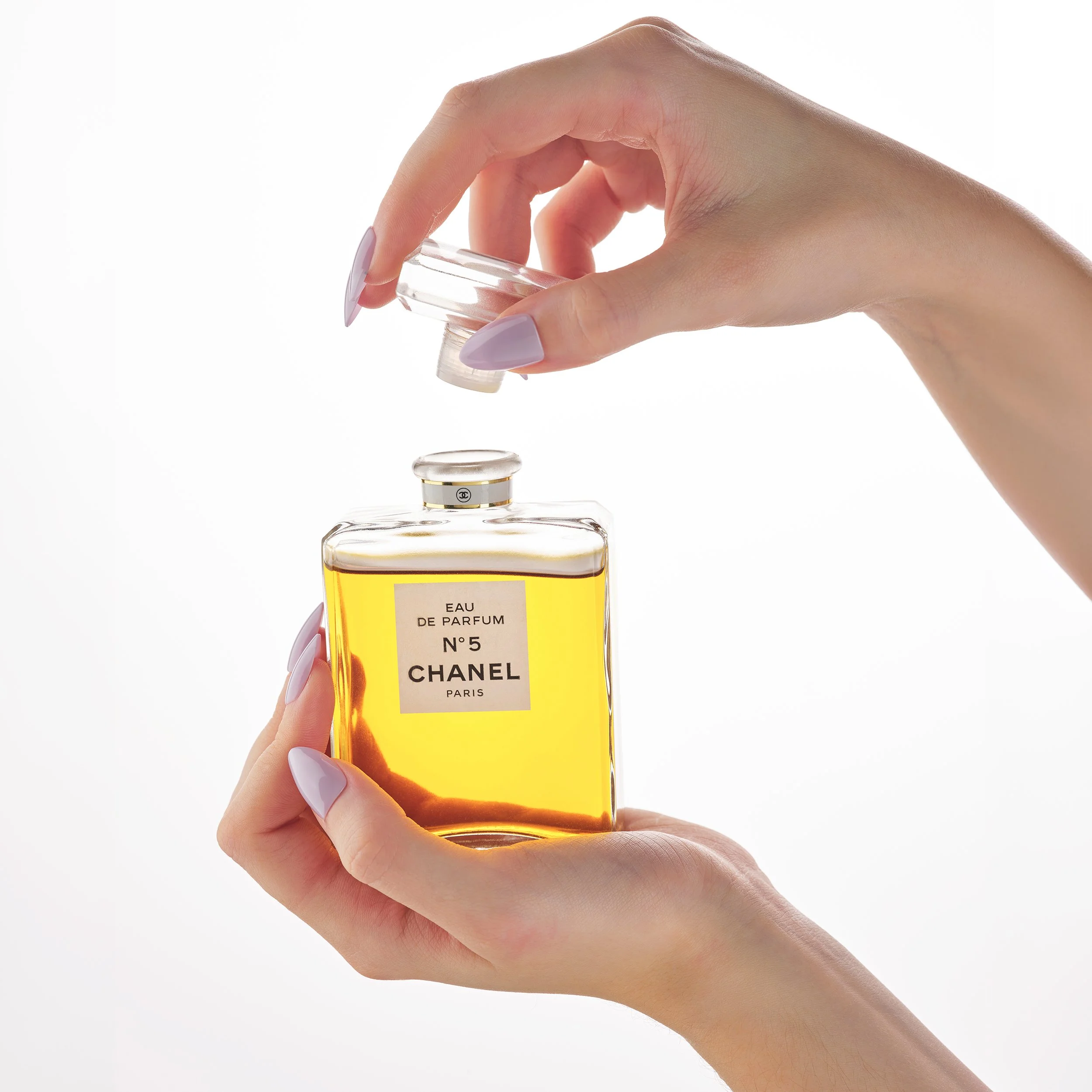 Hände, die ein Parfüm-Fläschchen mit Chanel No. 5 verwenden, vor weißem Hintergrund.