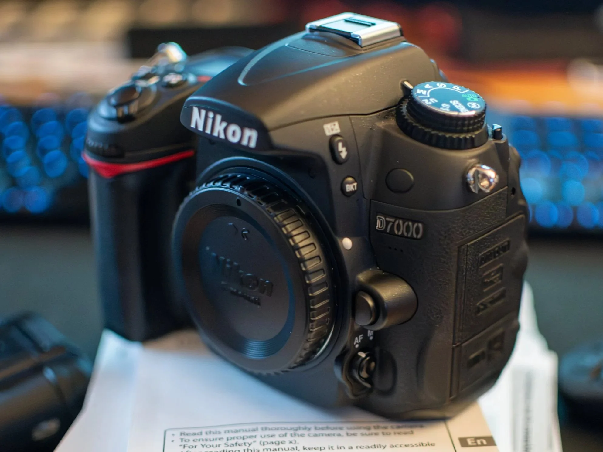 Close-up of a Nikon D7000 digital camera placed on a surface, with a focus on the top dials and controls.