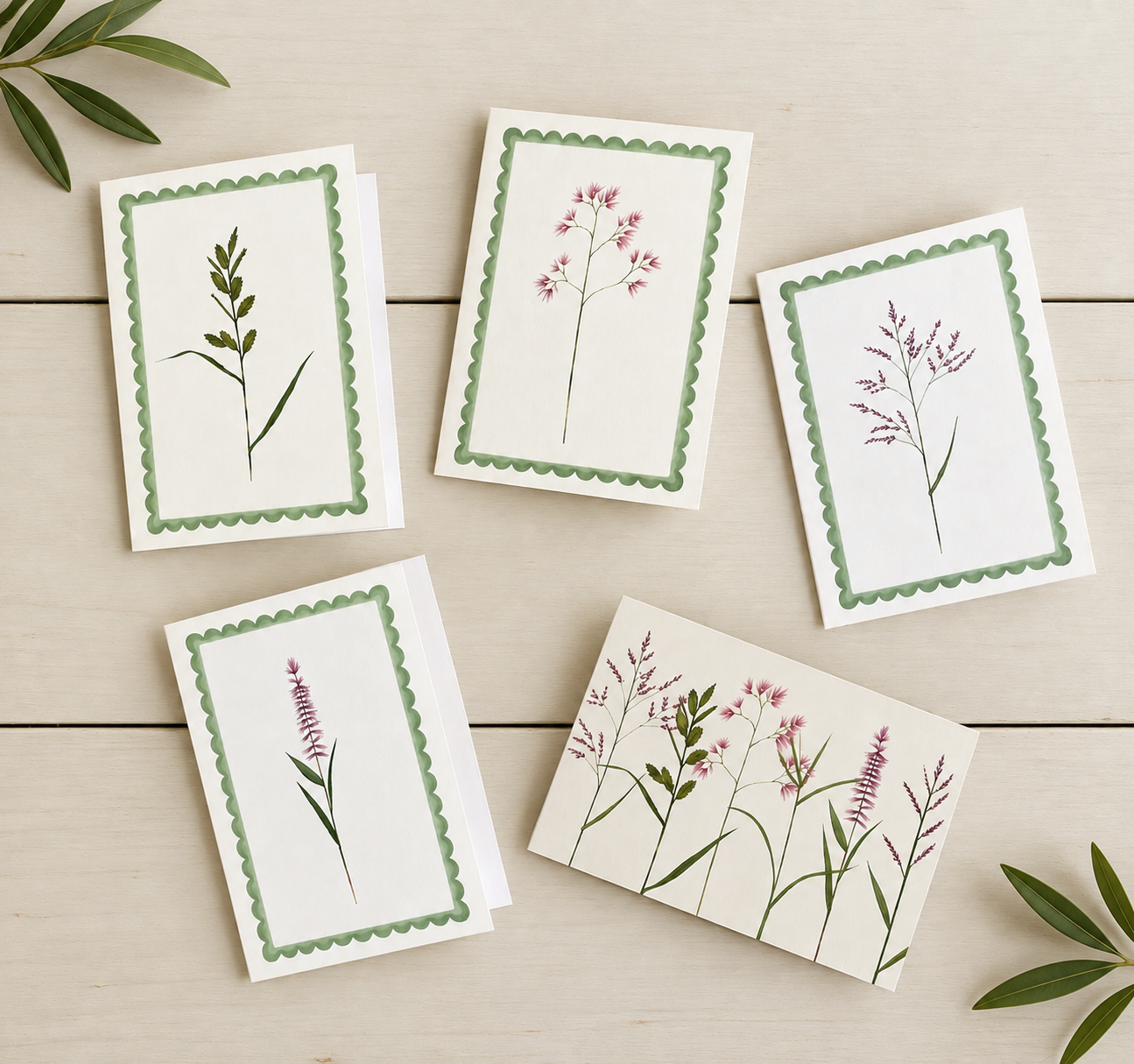 Collection of five botanical illustrations of various flowering plants placed on a light wooden surface, with some green leaves in the corners.