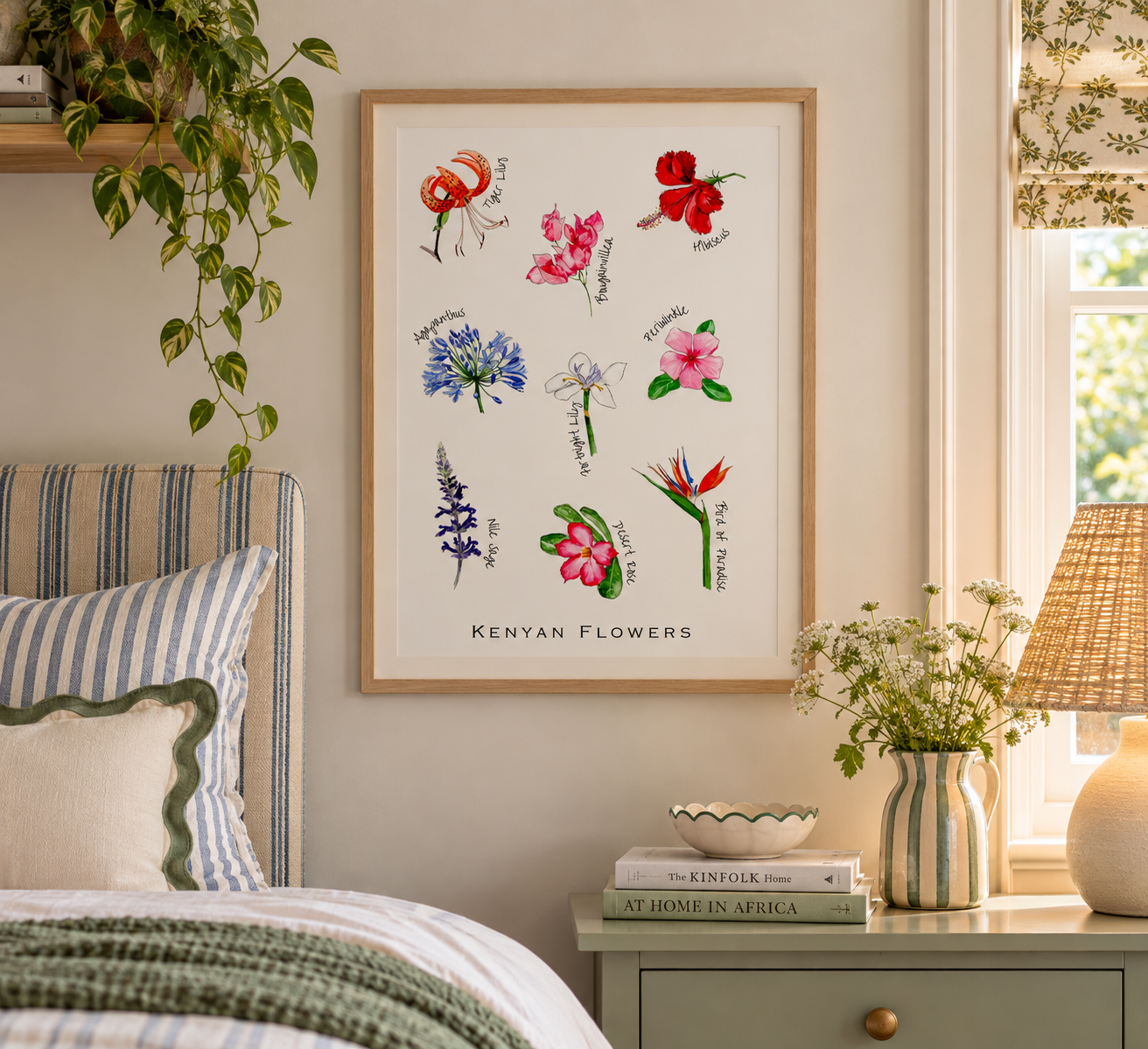 A framed poster of Kenyan flowers hangs on a wall above a bedside table with a plant, a ceramic bowl, and books. The room features natural lighting and cozy decor.
