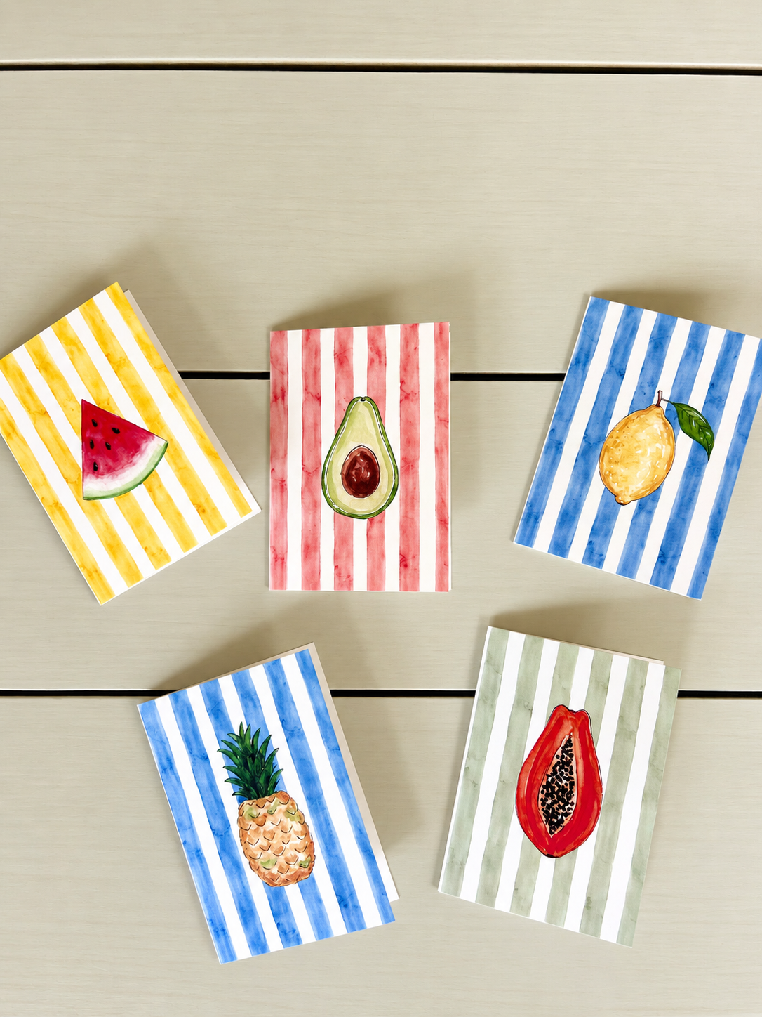 Watercolor illustrations of fruits on striped backgrounds, including watermelon, avocado, lemon, pineapple, and papaya, arranged on a light wooden surface.