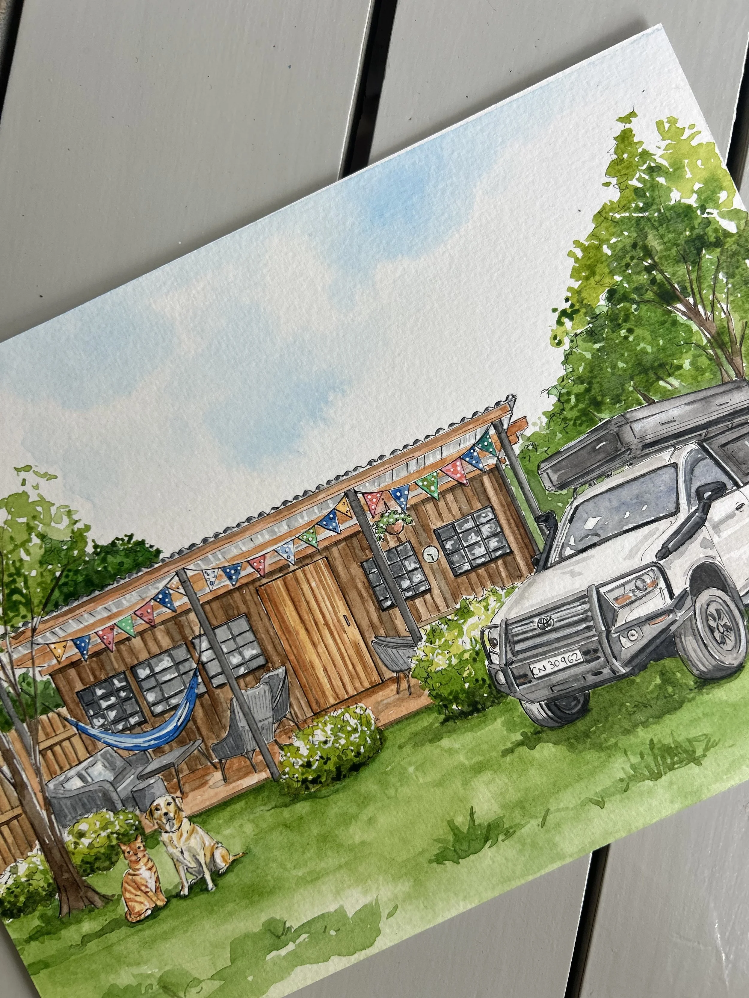 Watercolor painting of a backyard scene with a wooden shed, decorated with colorful flags, surrounded by green trees and grass. There are two dogs and a cat sitting near a tree, with a gray vehicle parked in the background.