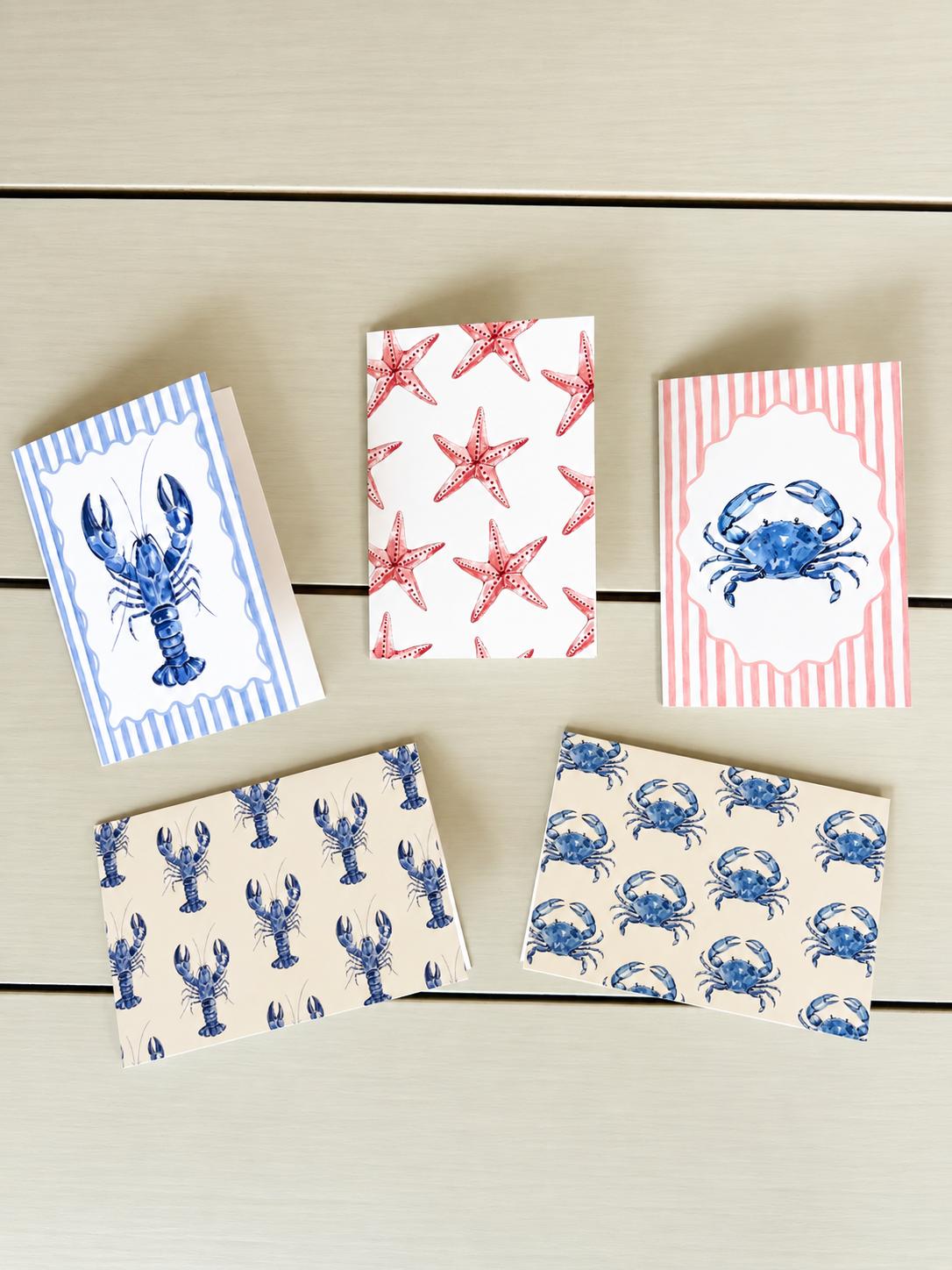 Six paper party napkins with seafood and starfish designs on a light wooden surface.