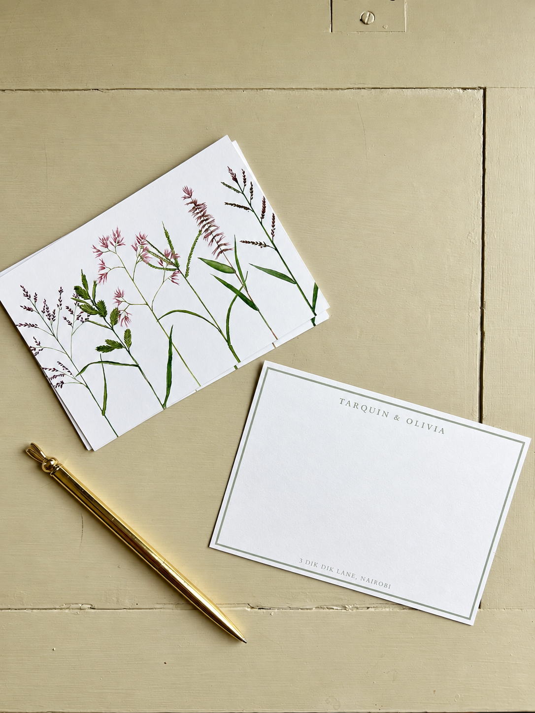 Invitation card with the names Tarquin and Olivia, a white envelope with botanical illustrations, and a gold pen on a beige surface.