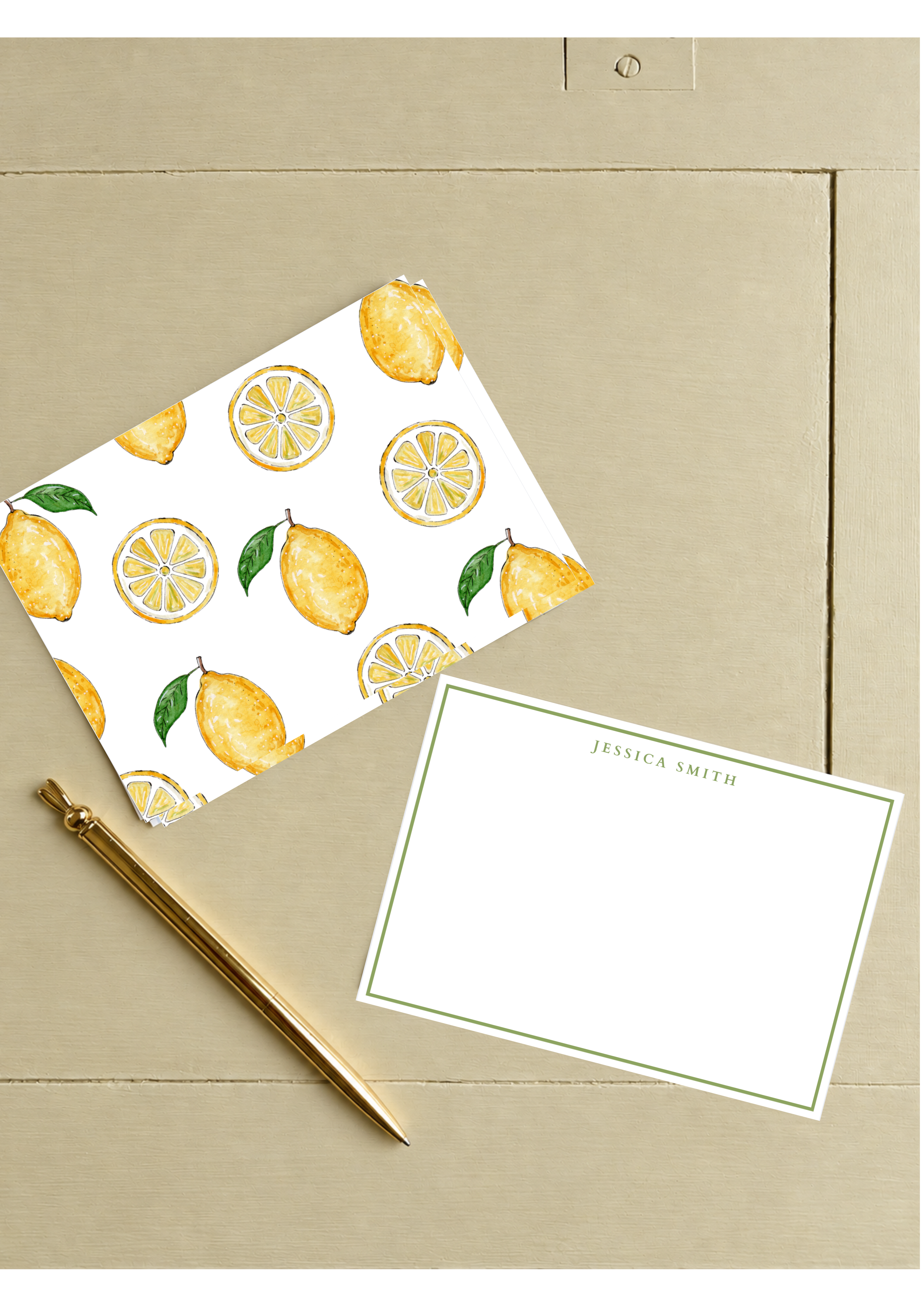Decorative stationery with lemon pattern, a gold pen, and a blank card with green border on a beige wooden surface.