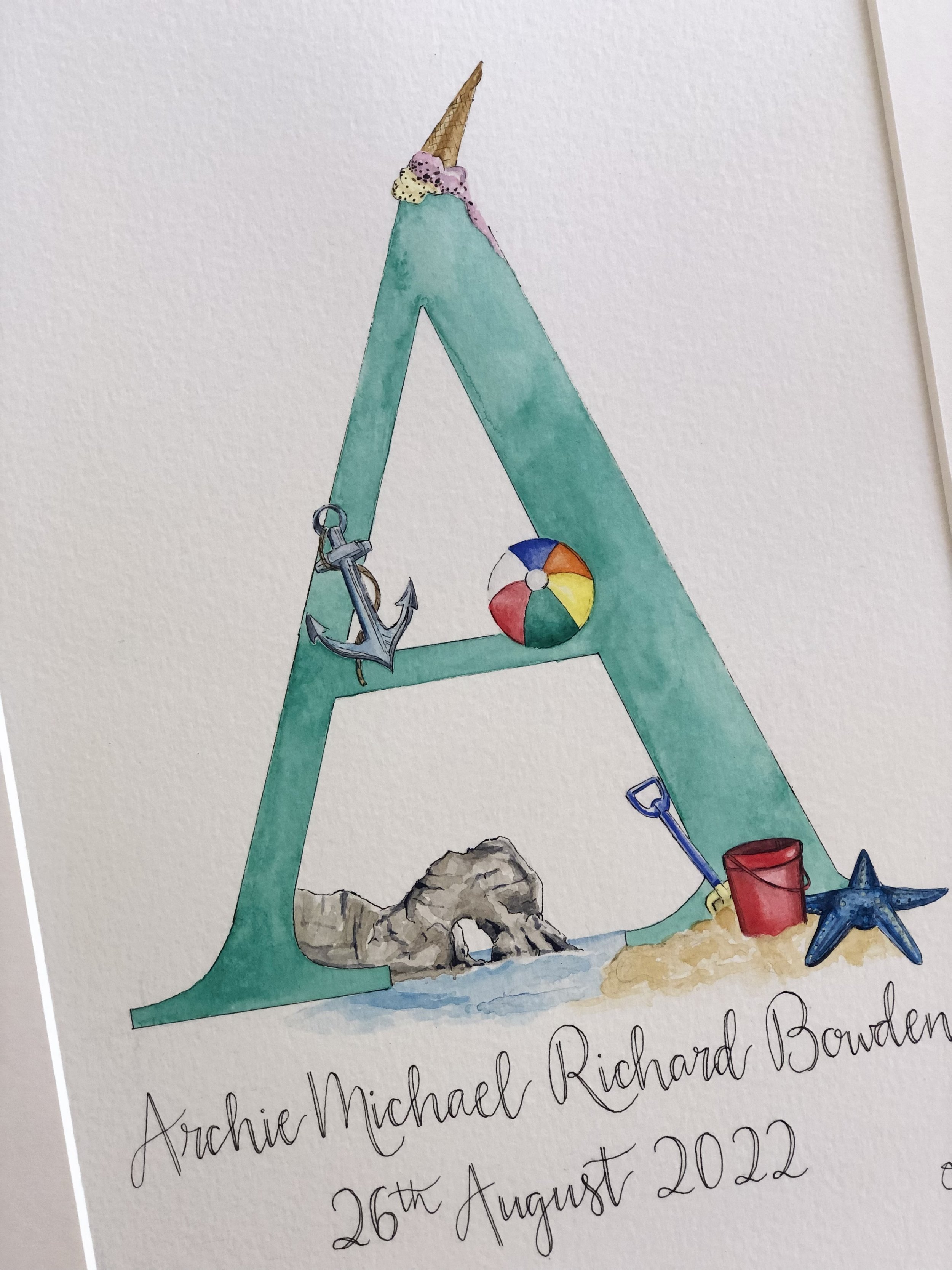 A watercolor painting of a beach scene with a large teal letter 'A' decorated with a brown ice cream cone, a colorful beach ball, an anchor, a shovel, a starfish, a red bucket, and a large rock, with handwritten text below reading 'Archie Michael Ric