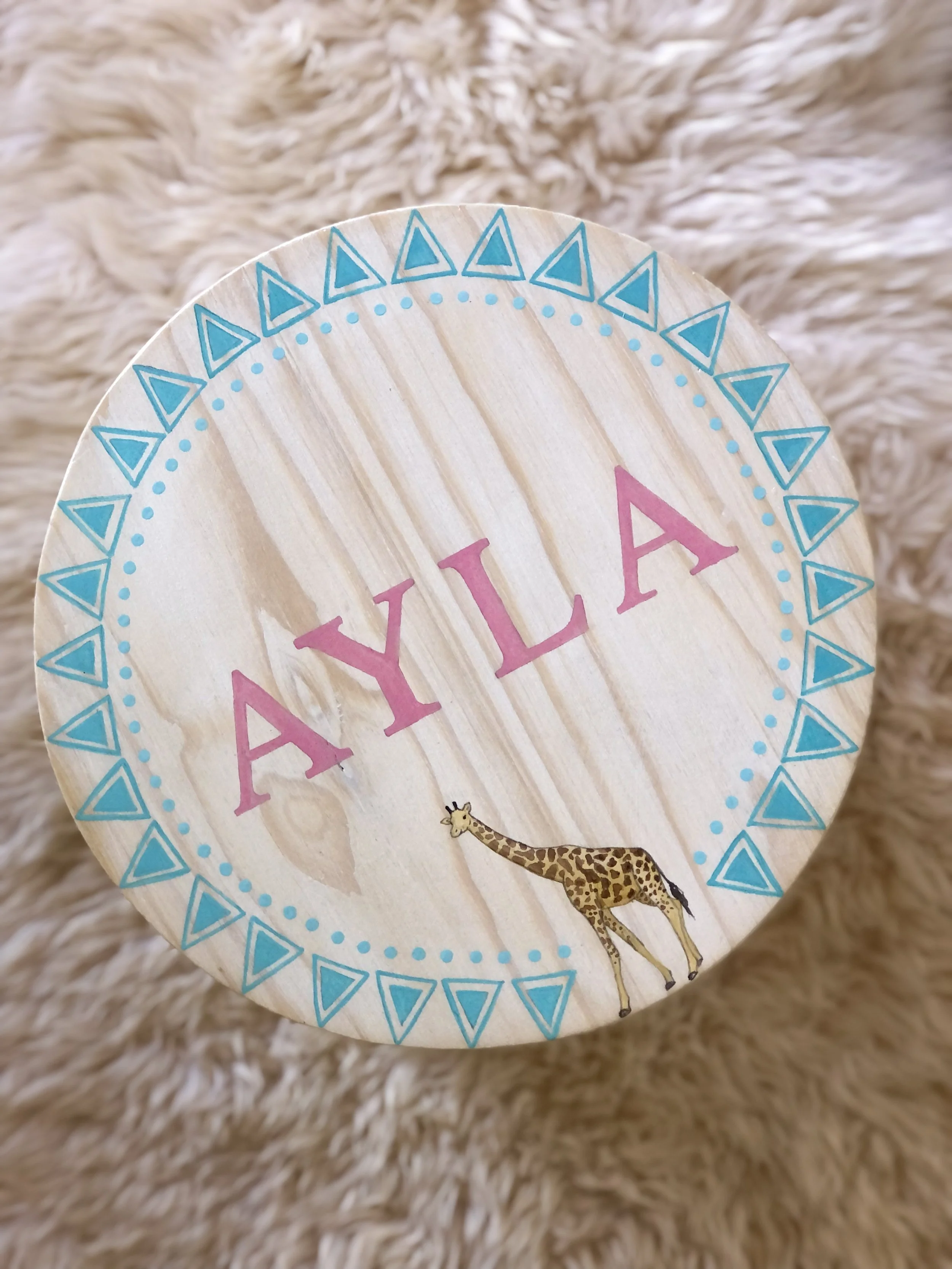 Part of a circular paper decoration with colorful printed patterns, including the word 'YAY' in pink letters and a small illustration of a giraffe, lying on a fluffy, cream-colored surface.