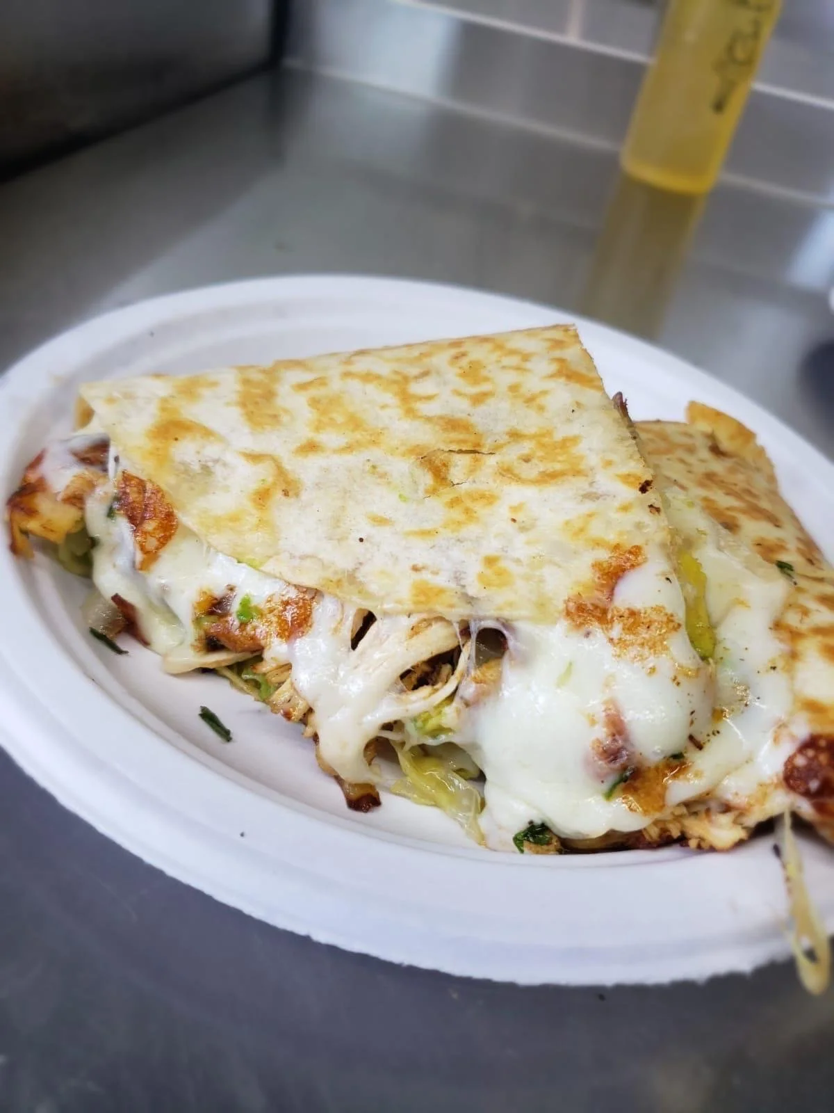 A close-up of a piece of pizza with melted cheese, vegetables, and a crispy flatbread on top, served on a white oval plate.