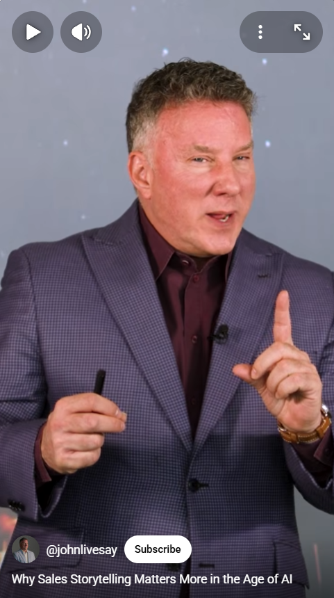 A man in a purple checkered suit and dark shirt is speaking, holding a pen in one hand and raising his index finger.