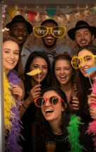 Group of friends having fun with props at an open-air photo booth during a celebration.