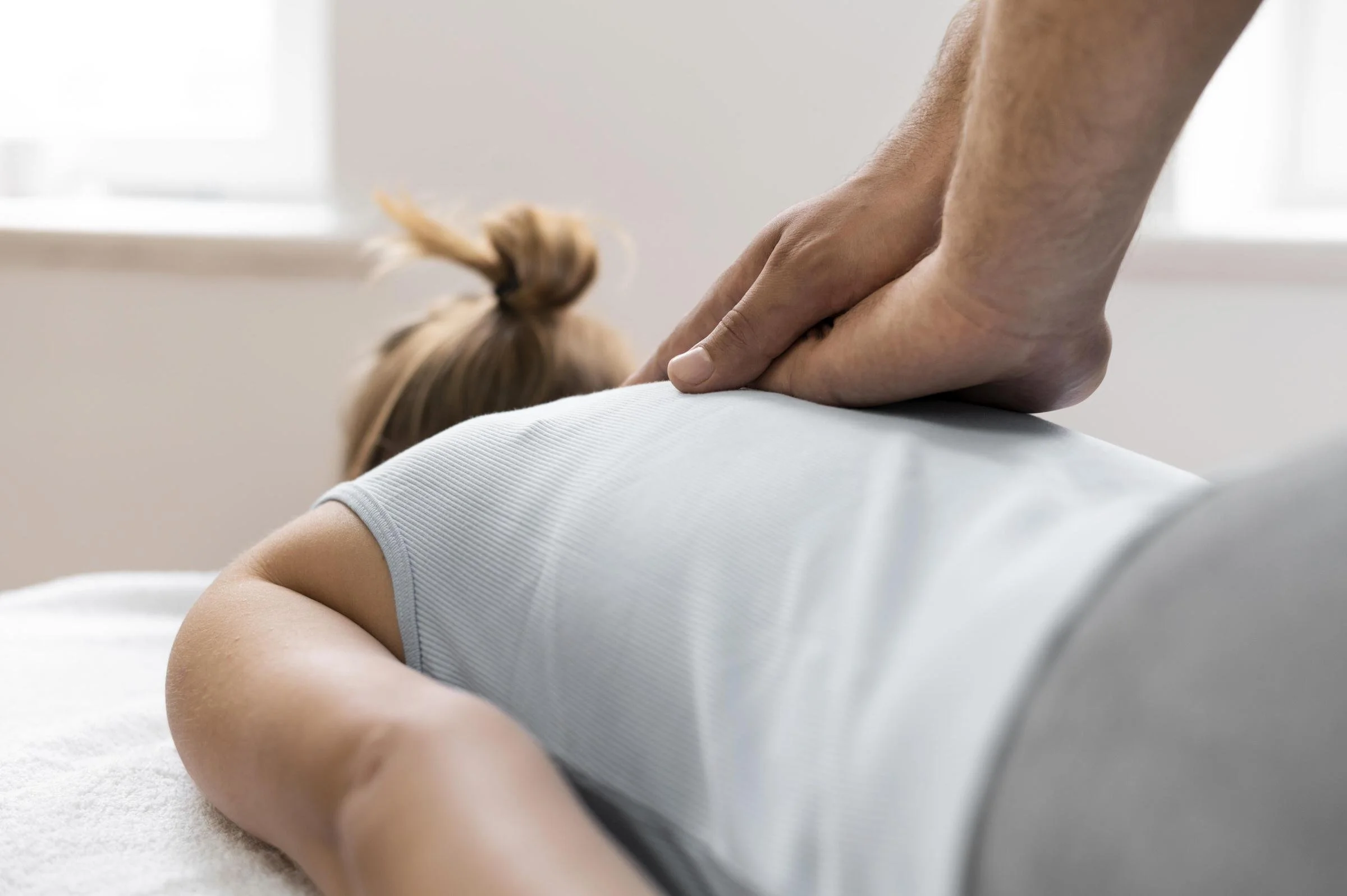 A person receiving a back massage from an osteopathic physician in a bright room.