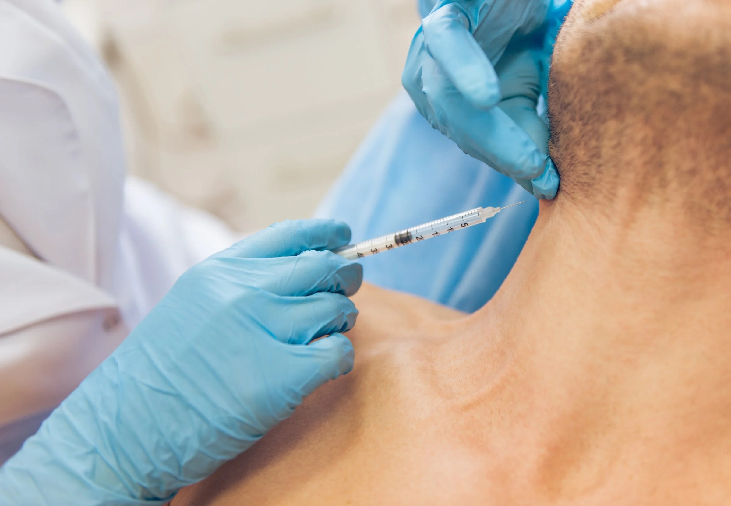 An osteopathic physician wearing blue gloves administering an injection into a patient's chest area using a syringe.