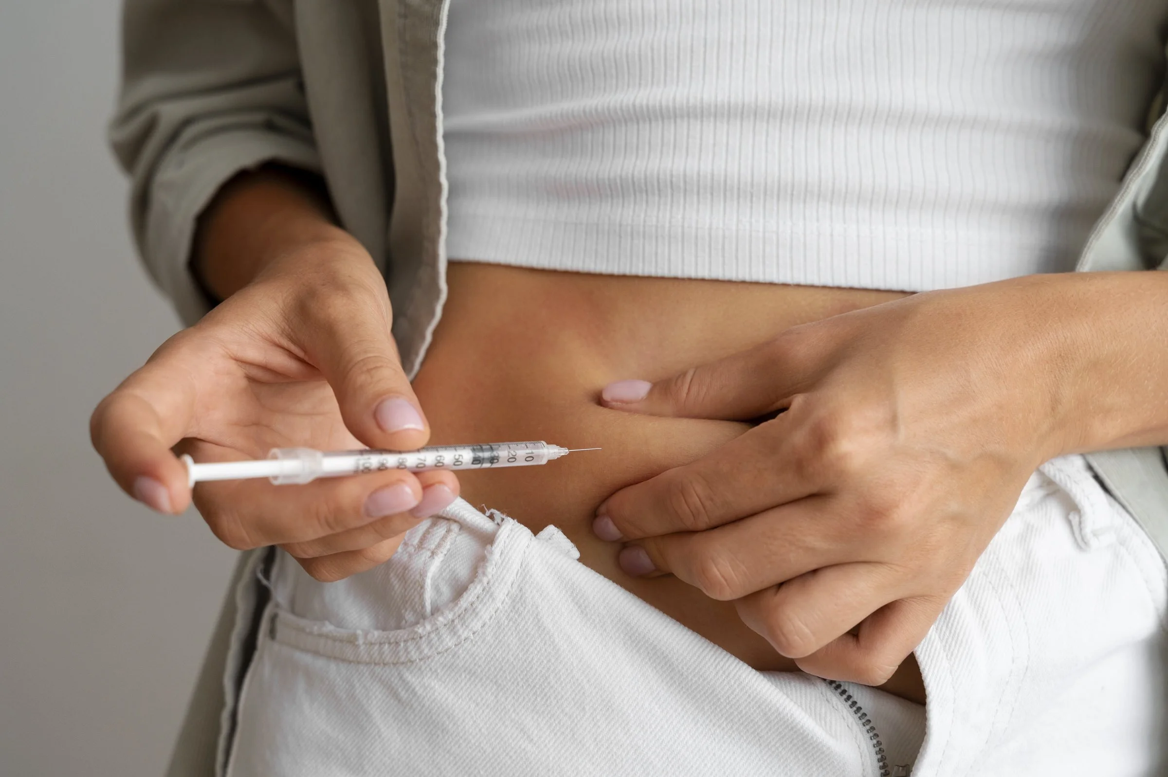 Person receiving an injection in their abdominal area, with hands holding and administering the shot.