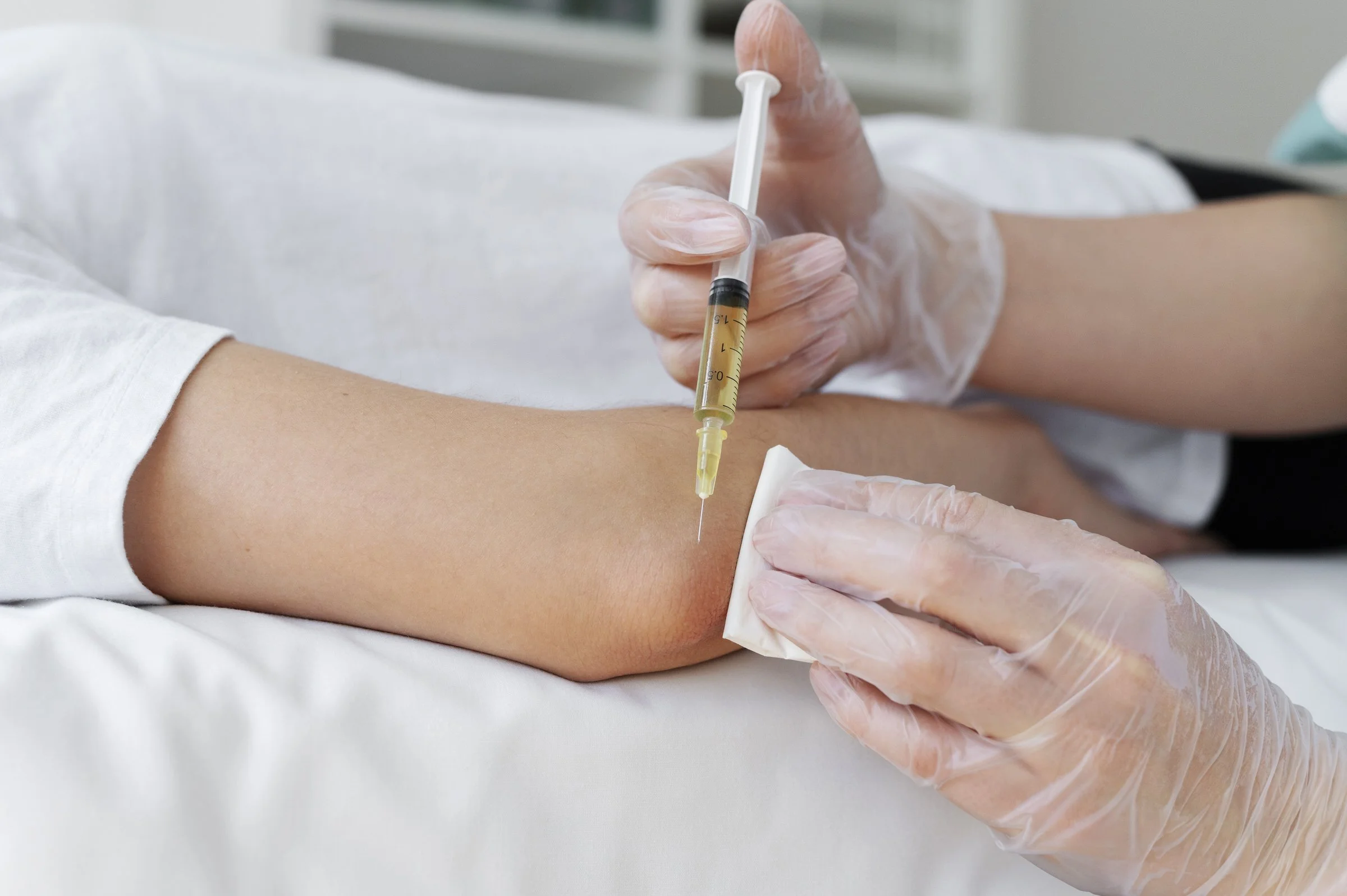 A healthcare professional administering an injection into a patient's arm, hand wearing a glove, using a syringe.